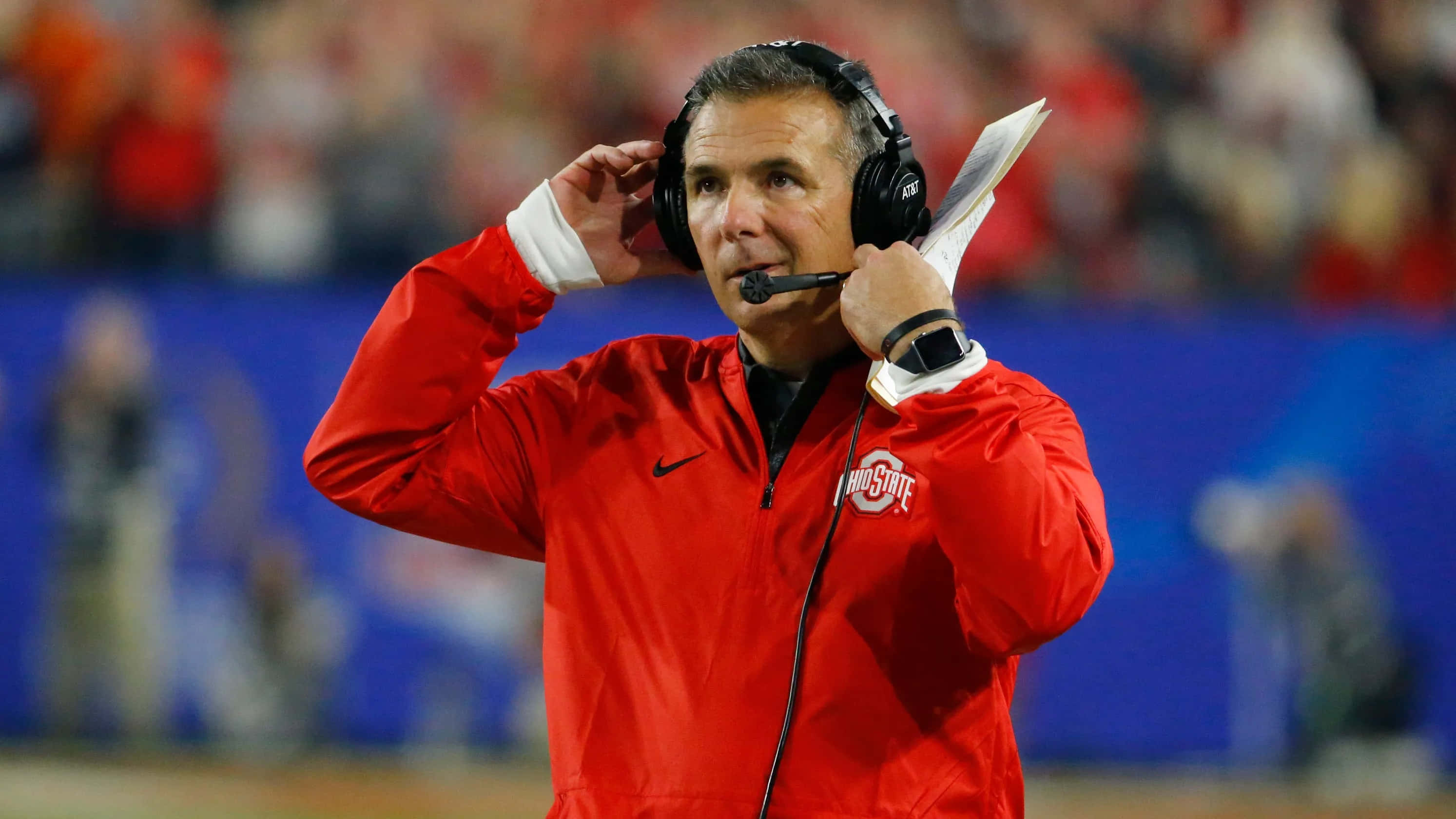 Urban Meyer 桌布 壁紙 — 一名身穿紅色俄亥俄州立大學外套的足球教練在比賽期間於邊線調整耳機。