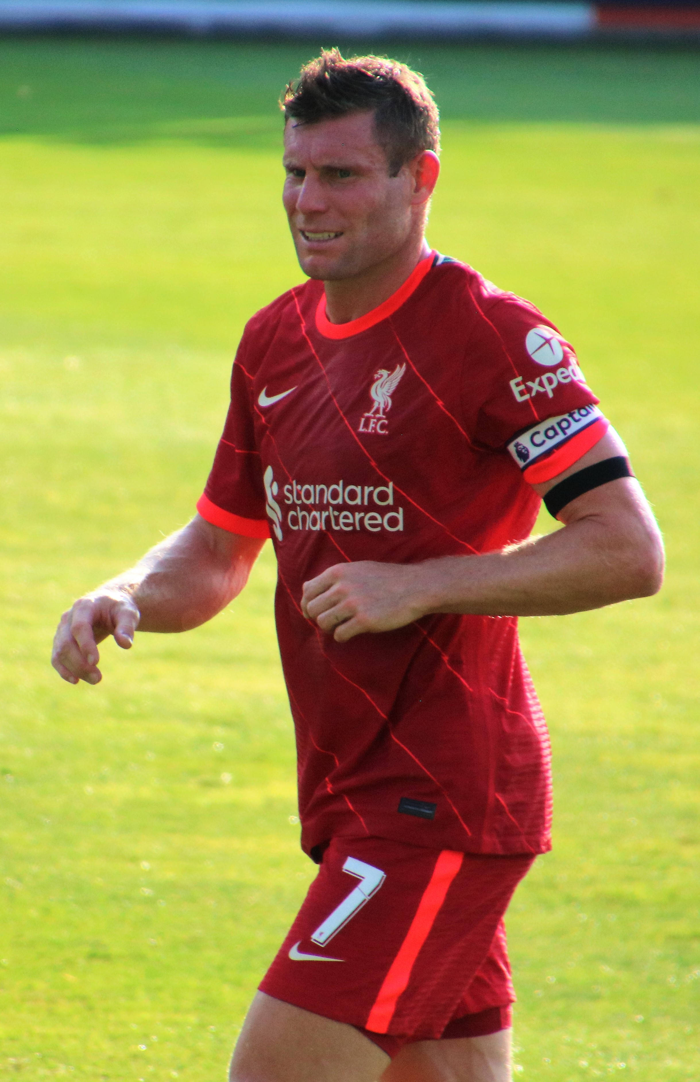 Liverpool Fc 桌布 壁紙 — 一名身穿紅色利物浦球衣的足球員在陽光明媚的綠色球場上專注地奔跑。