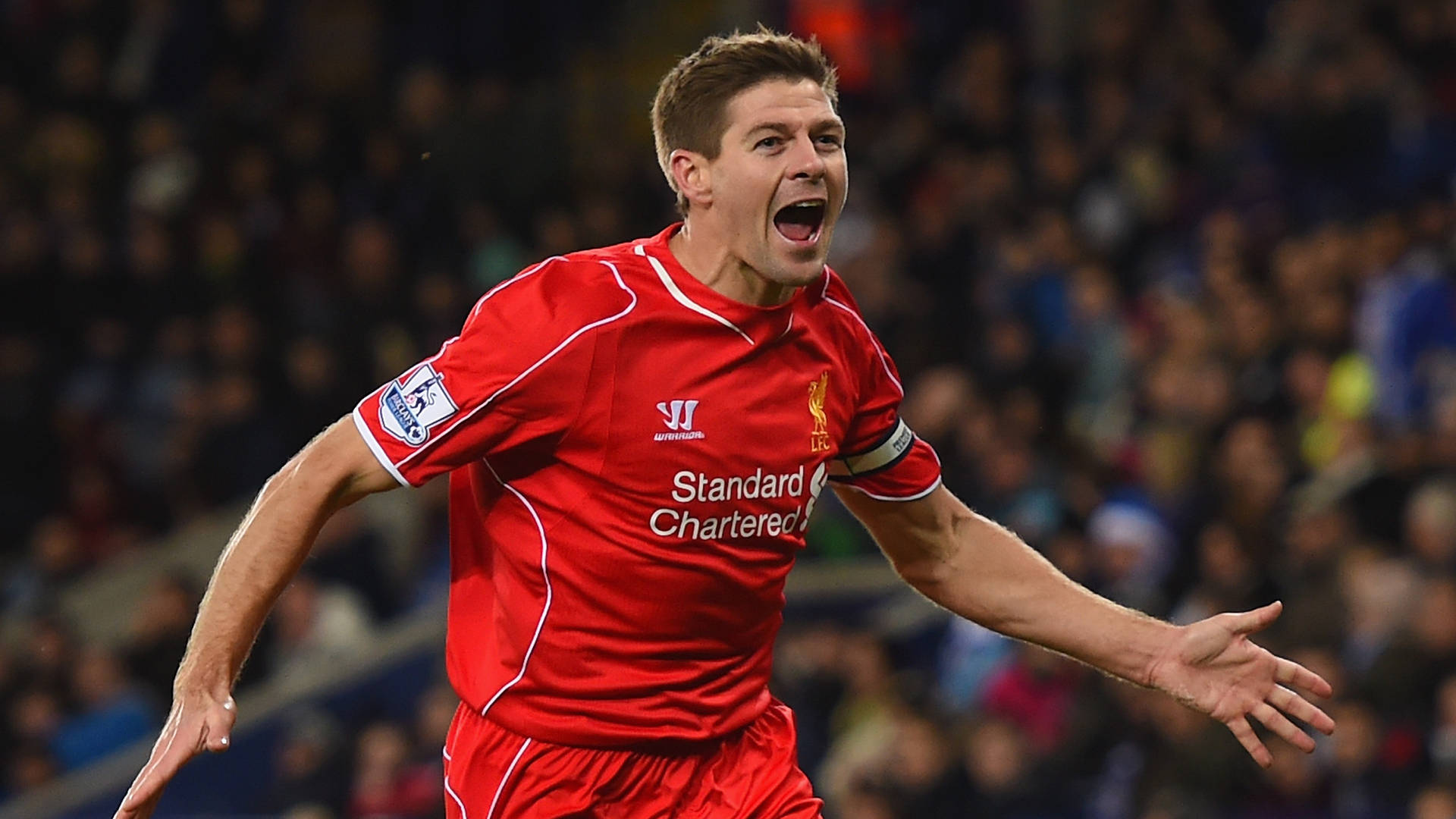 Steven Gerrard 桌布 壁紙 — 一名身穿紅色利物浦球衣的足球員在球場人群中熱情地張開雙臂慶祝。