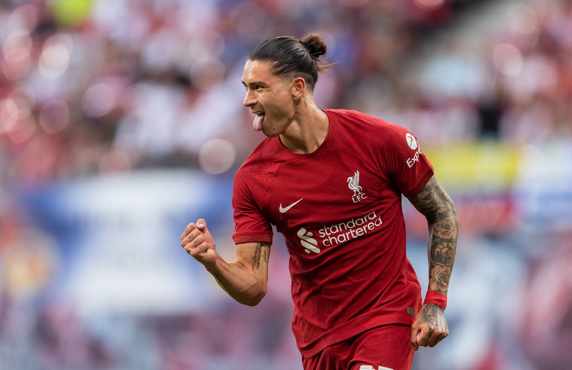 Liverpool Fc 桌布 壁紙 — 一名身穿紅色利物浦球衣的足球員在陽光明媚的球場上伸出舌頭、握緊拳頭慶祝。