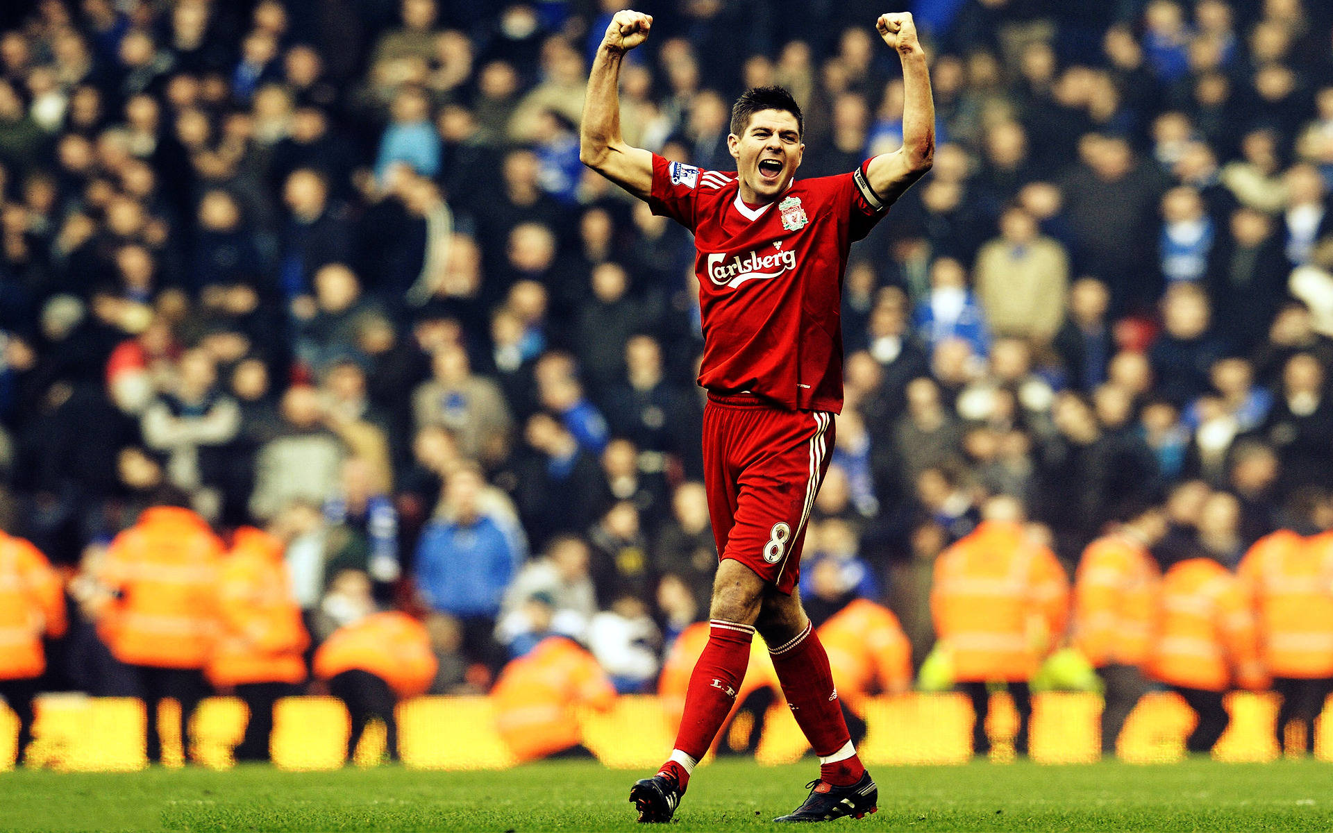 Steven Gerrard 桌布 壁紙 — 一名身穿紅色利物浦球衣的足球運動員在球場的泛光燈下高舉拳頭慶祝勝利。