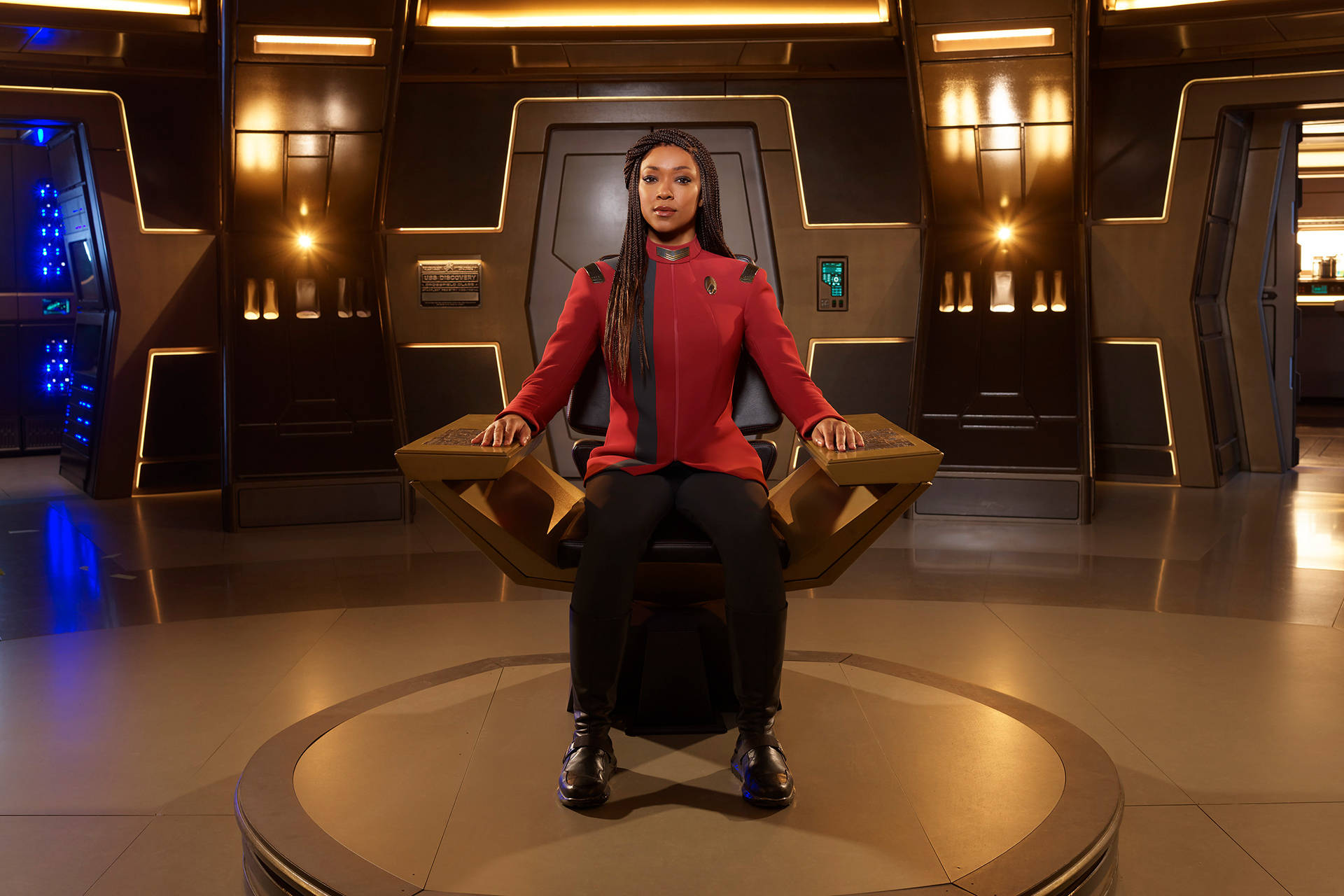 Discovery 桌布 壁紙 — 一名身穿紅色制服的星際艦隊軍官，在充滿溫暖金色光線的未來太空船艦橋上，坐在指揮官椅上。