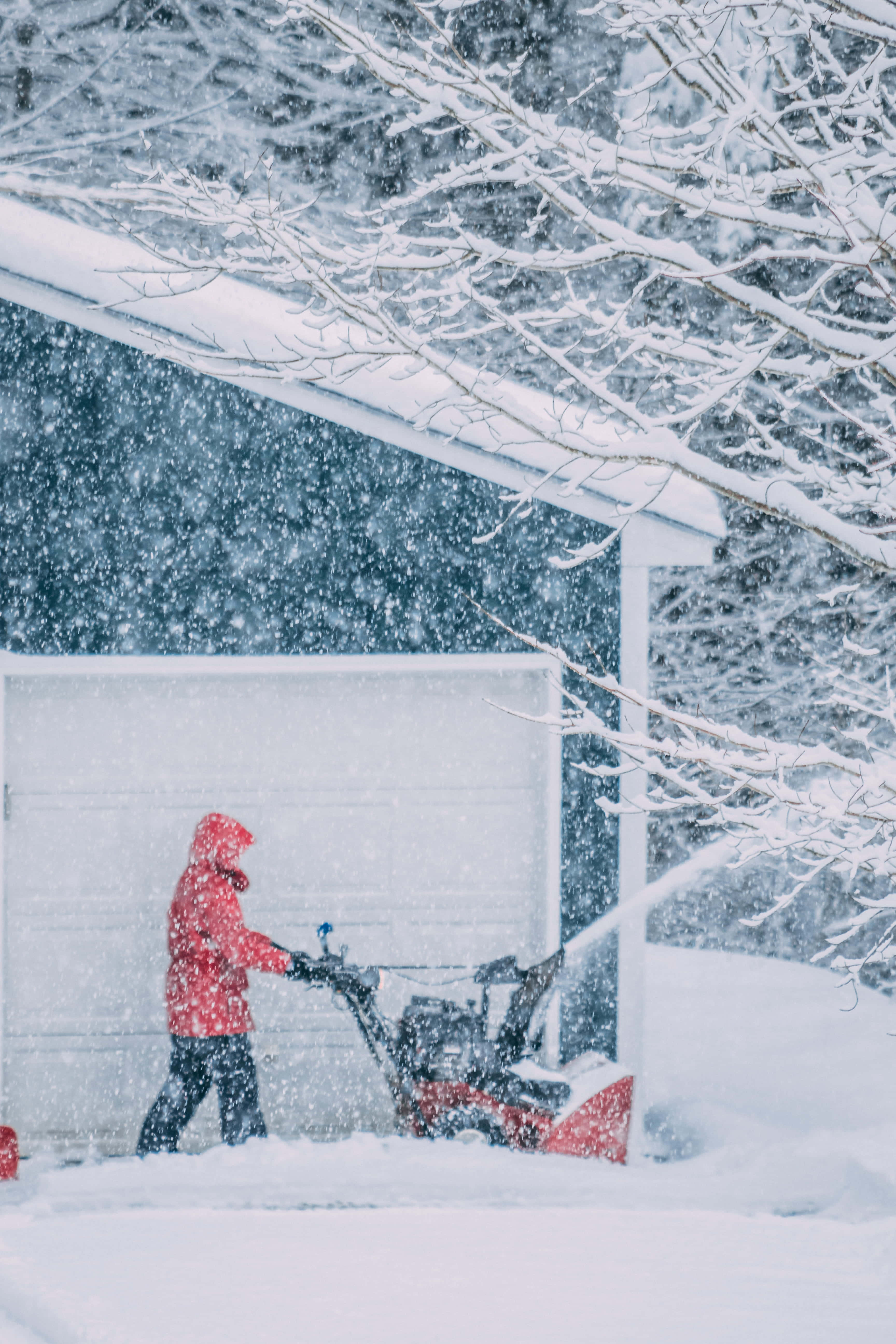 Snowplow 桌布 壁紙 — 一名身穿紅色外套的人在大雪中從車庫旁的車道鏟雪。