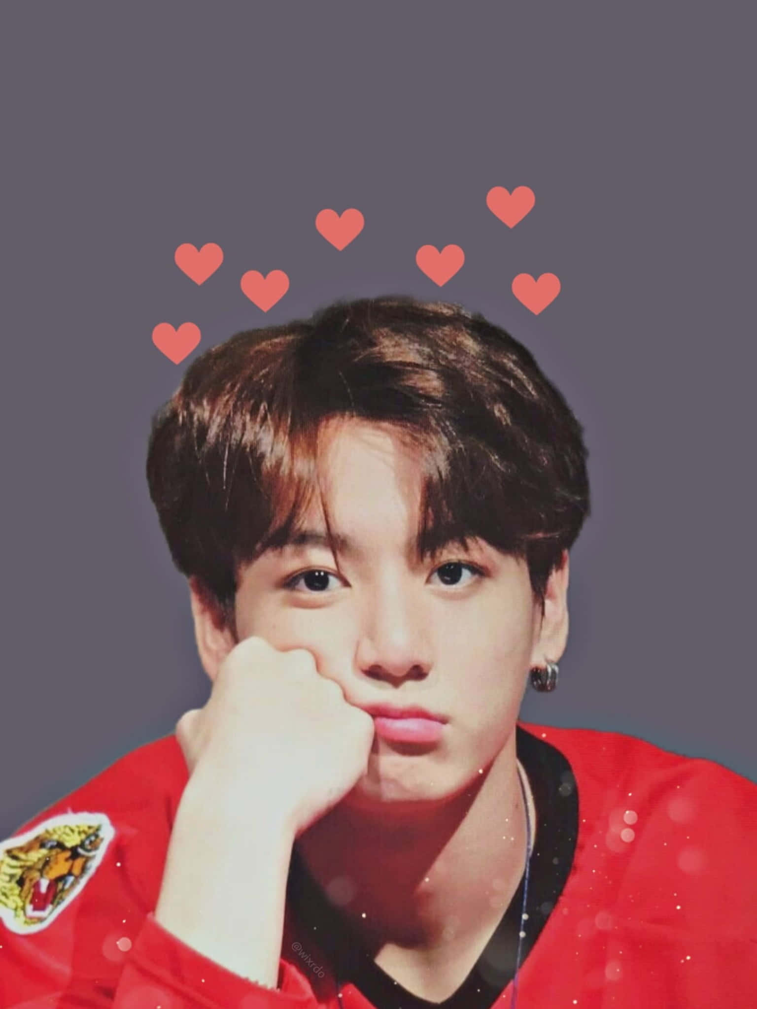 Jungkook 桌布 壁紙 — 一名身穿紅色外套的年輕男子，手托下巴，頭頂上方漂浮著心形圖案，背景為灰色。