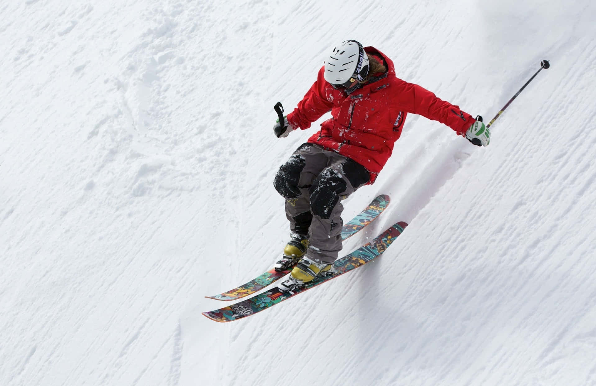 ski 桌布 壁紙 — 一名身穿紅色外套的滑雪者，在雪坡上以動態動作和雪花飛濺的方式滑下。