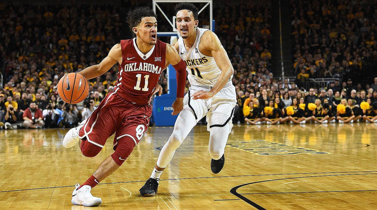 Trae Young 桌布 壁紙 — 一名身穿紅色奧克拉荷馬球衣的籃球運動員，在明亮的場館燈光下，運球越過一名身穿白色球衣的防守球員，進行一場激烈的比賽。