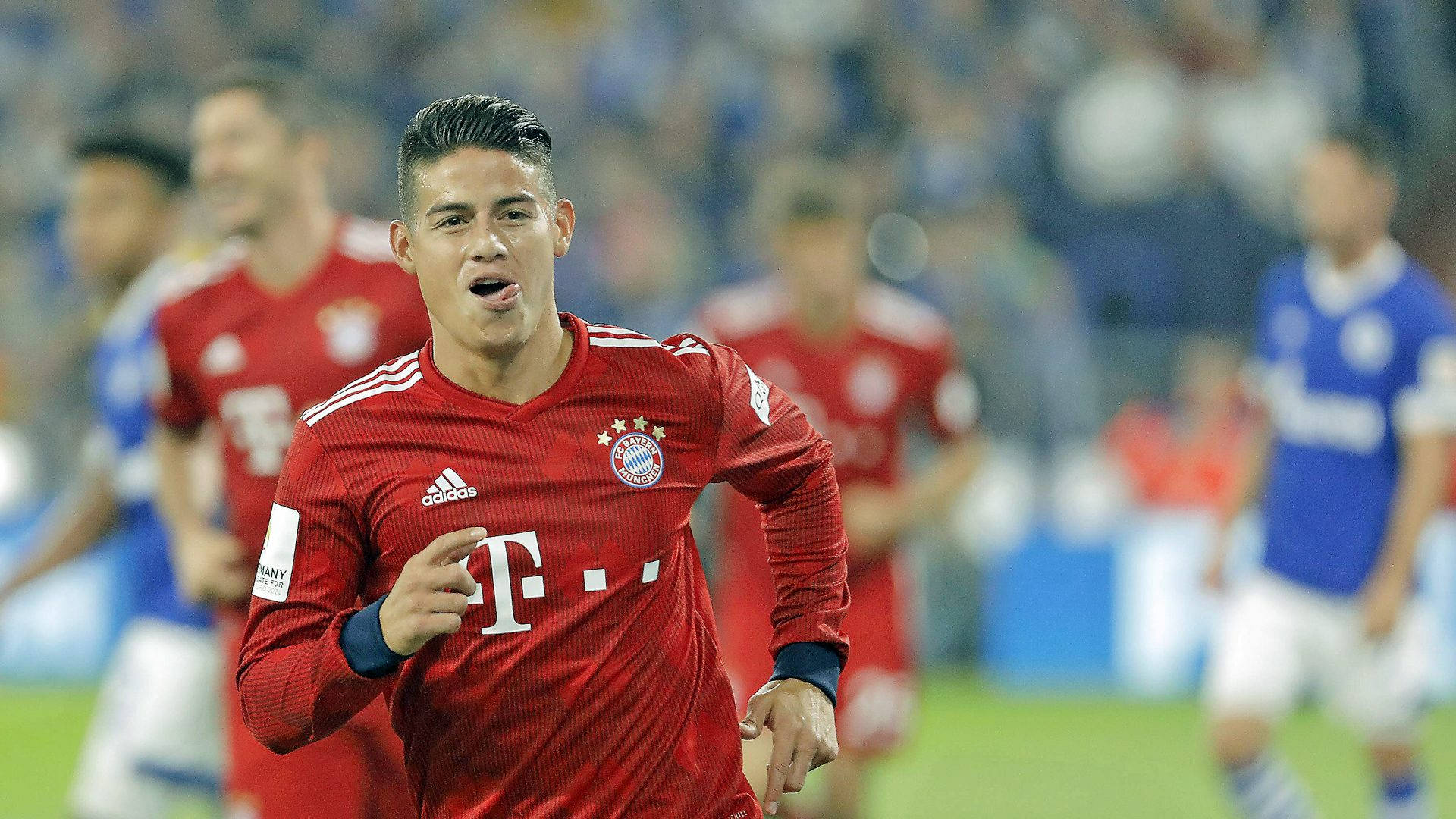 James Rodriguez 桌布 壁紙 — 一名身穿紅色拜仁慕尼黑球衣的足球運動員在燈火通明的球場上激烈慶祝。