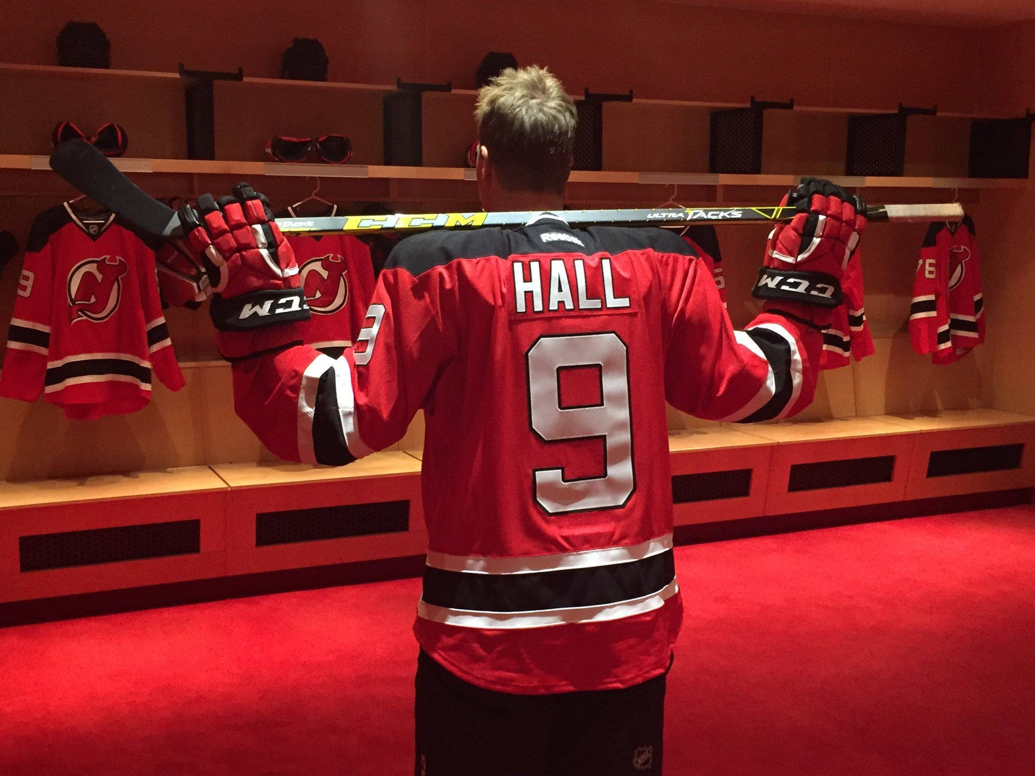 hockey 桌布 壁紙 — 一名身穿紅色新澤西惡魔隊球衣、印有Hall名字和9號的冰球運動員，站在更衣室裡，手持球桿和手套。
