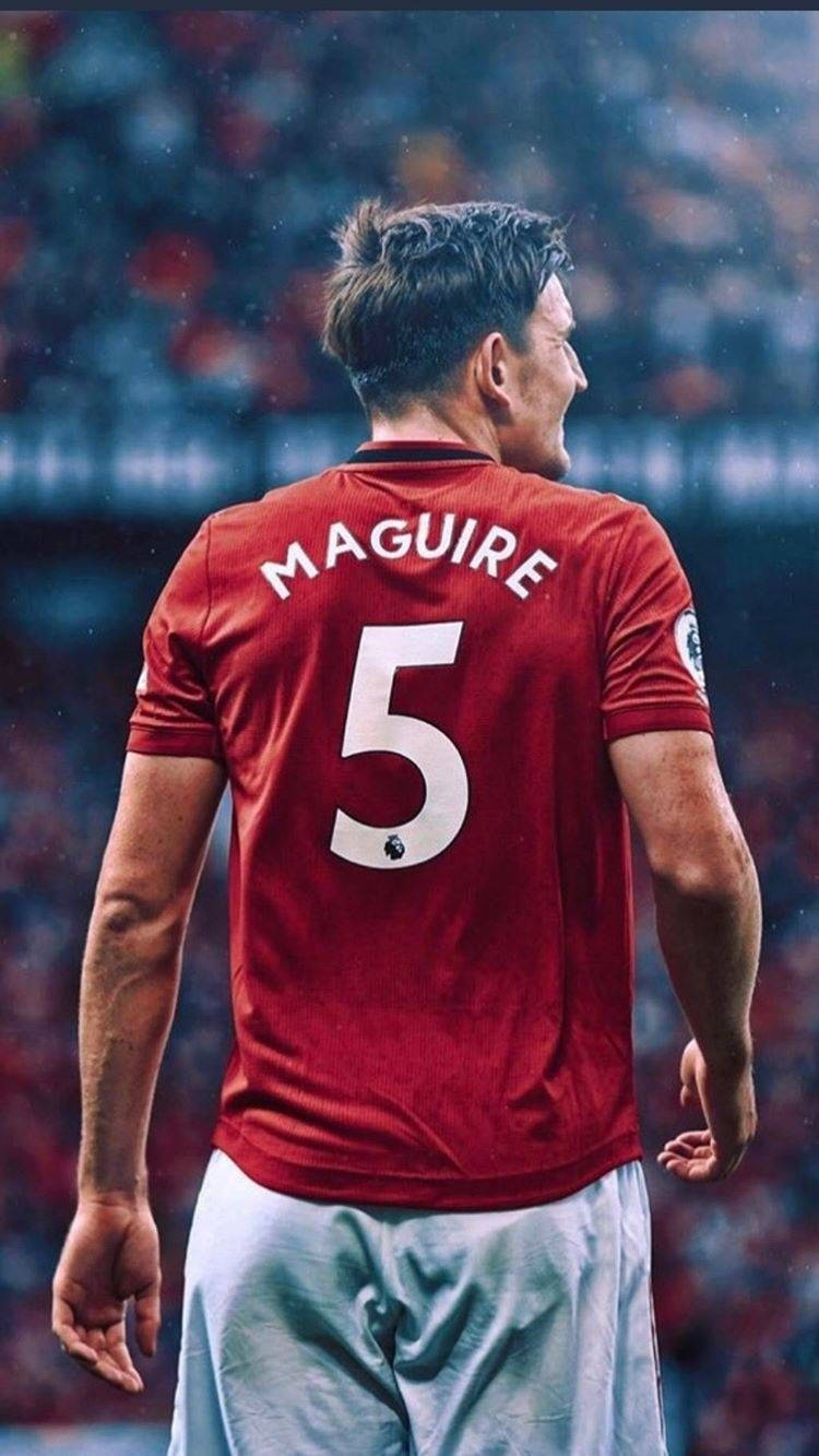 運動 桌布 壁紙 — 一名身穿紅色曼聯球衣、背後印有「MAGUIRE 5」的足球員，在雨中球場背對鏡頭站立。