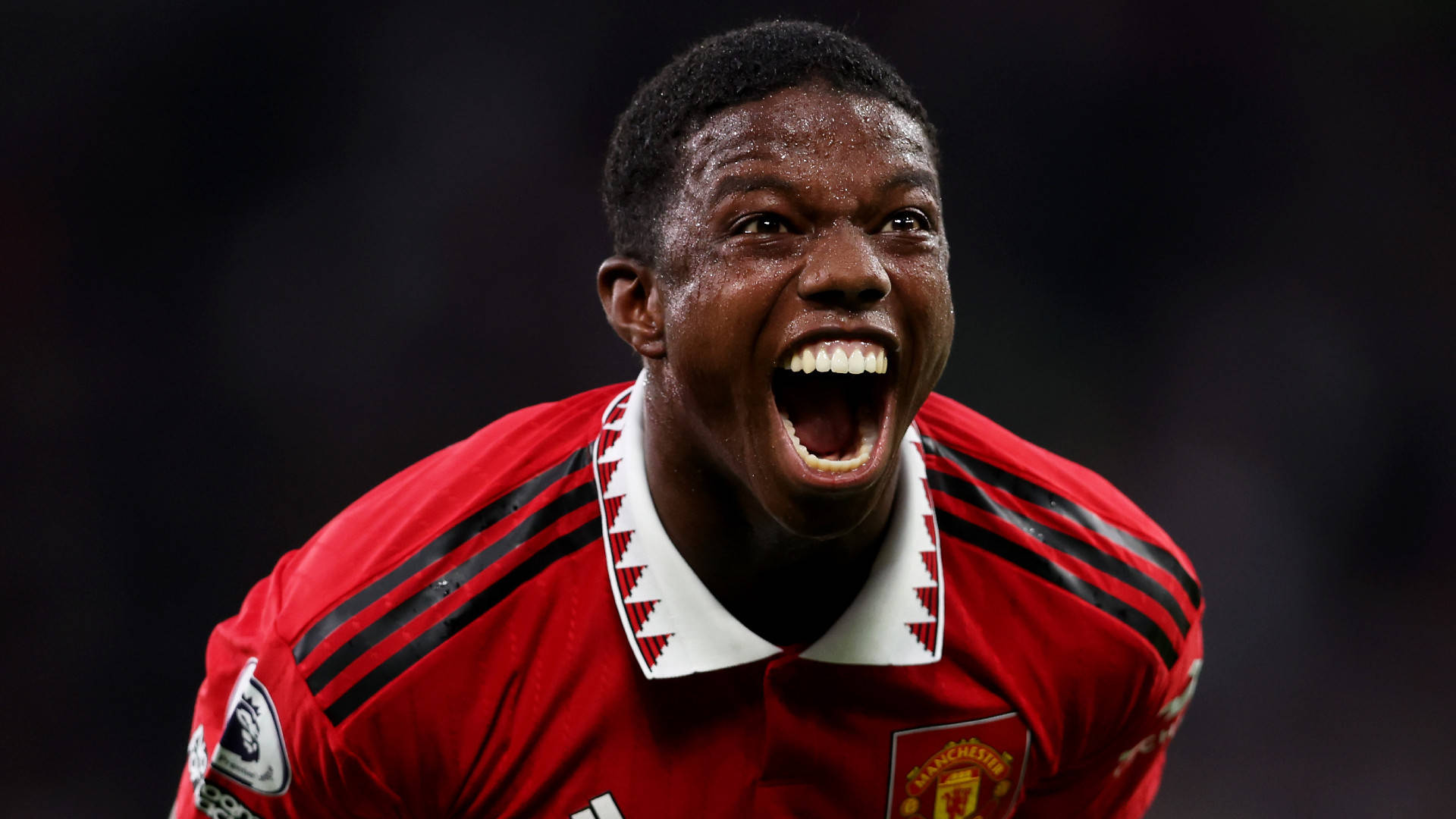Manchester United Logo 桌布 壁紙 — 一名身穿紅色曼聯球衣的足球員，臉上閃爍著汗水，發出勝利的吶喊。
