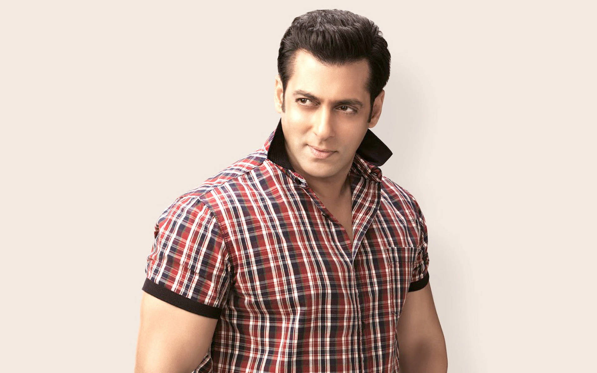 Salman Khan 桌布 壁紙 — 一名身穿紅色格紋襯衫的男子，在純米色背景前自信地擺姿勢，並有直接的眼神接觸。