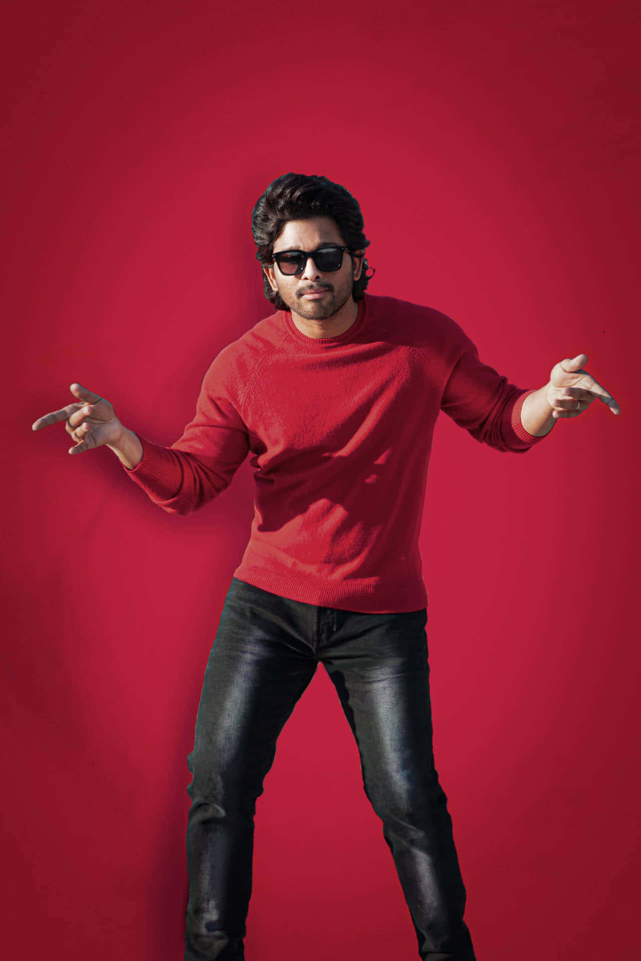 Allu Arjun 桌布 壁紙 — 一名身穿紅色毛衣、戴著太陽眼鏡的男子，在純紅色攝影棚背景前擺出自信姿勢。