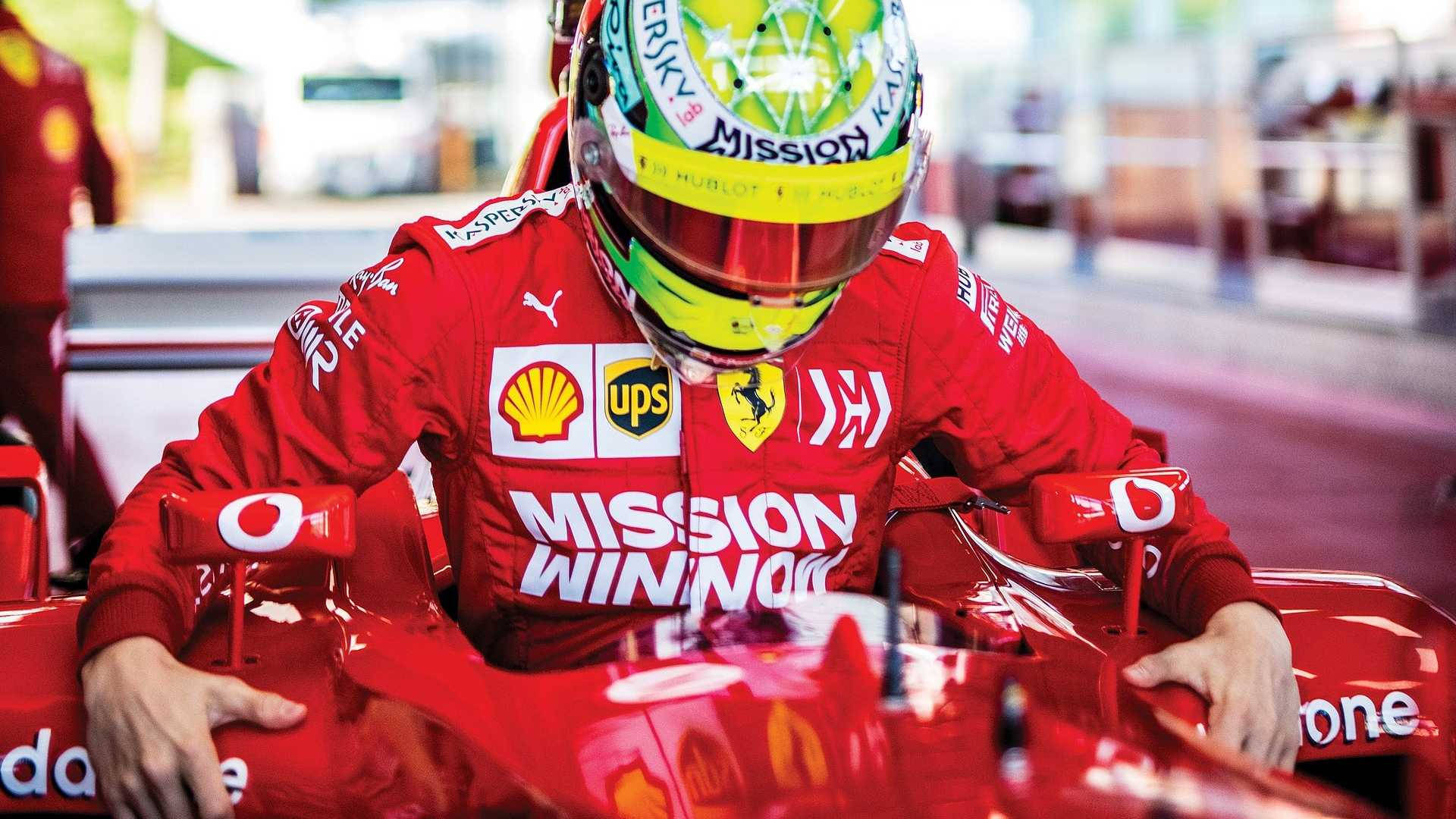 mick schumacher 桌布 壁紙 — 一名身穿紅色法拉利賽車服和頭盔的F1車手坐在帶有贊助商標誌的紅色賽車內。