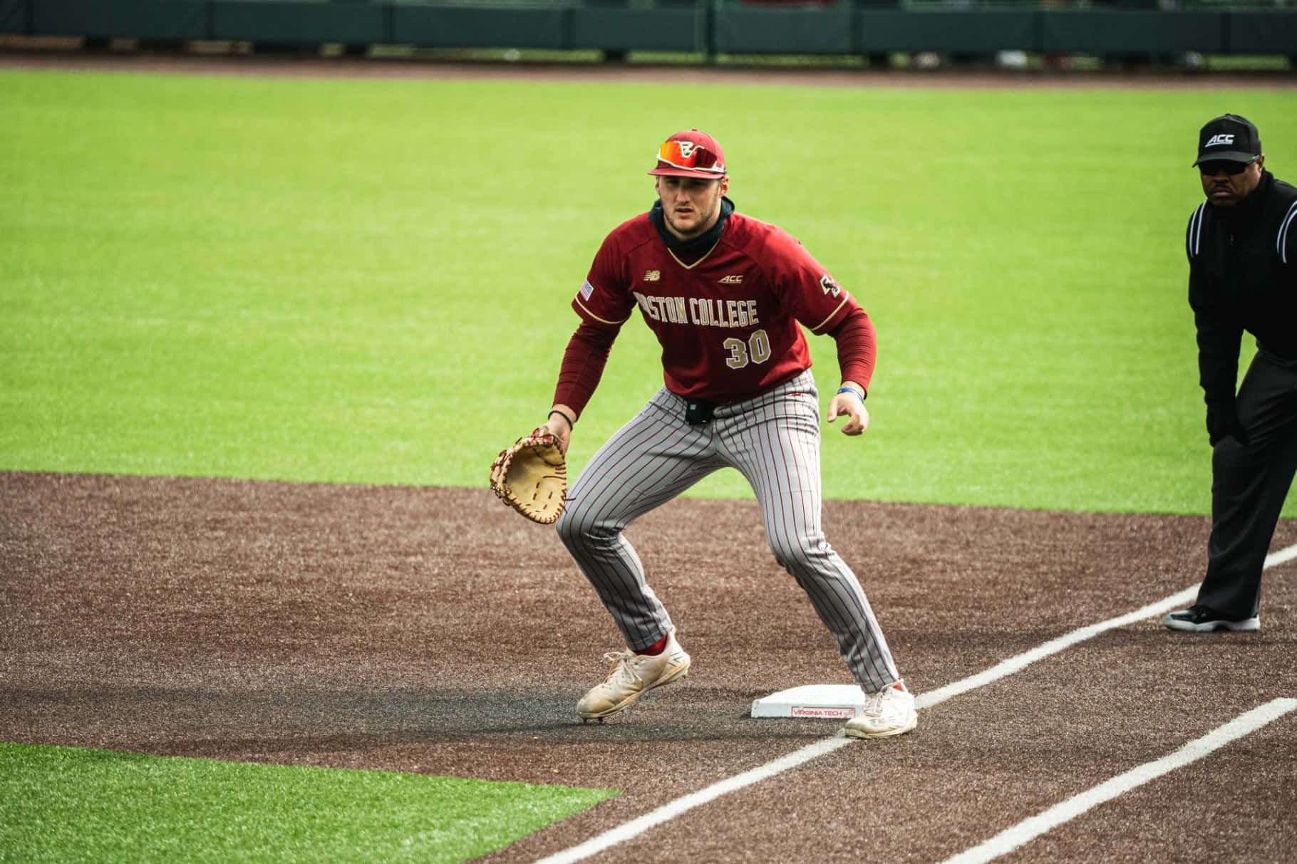 College Baseball 桌布 壁紙 — 一名身穿紅色波士頓學院球衣的棒球選手在日間比賽中蹲在壘包附近準備防守。