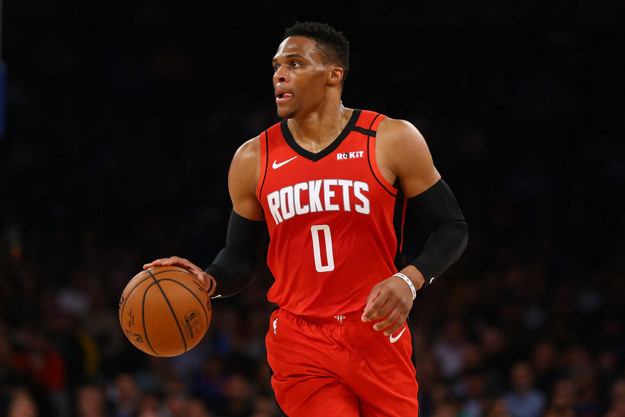 Westbrook 桌布 壁紙 — 一名身穿紅色火箭隊球衣的籃球運動員在場館燈光下專注地運球。