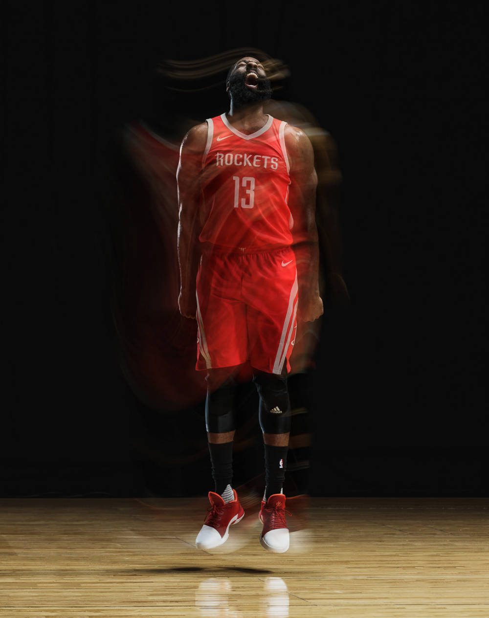 James Harden 桌布 壁紙 — 一名身穿紅色火箭隊球衣的籃球運動員在深色工作室背景的木地板上跳躍，帶有動態模糊效果。