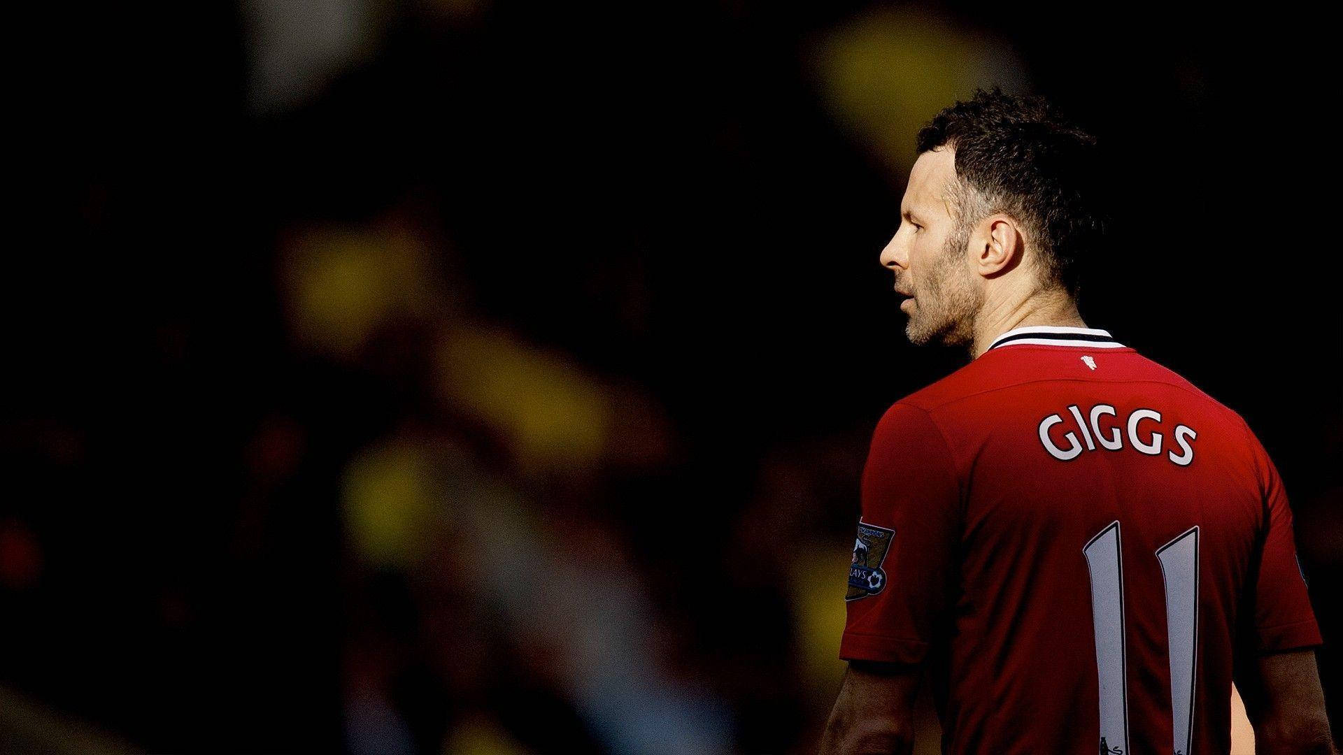 Ryan Giggs 桌布 壁紙 — 一名身穿紅色球衣、背後印有「GIGGS」和11號的足球員，側面站在黑暗模糊的球場背景下。