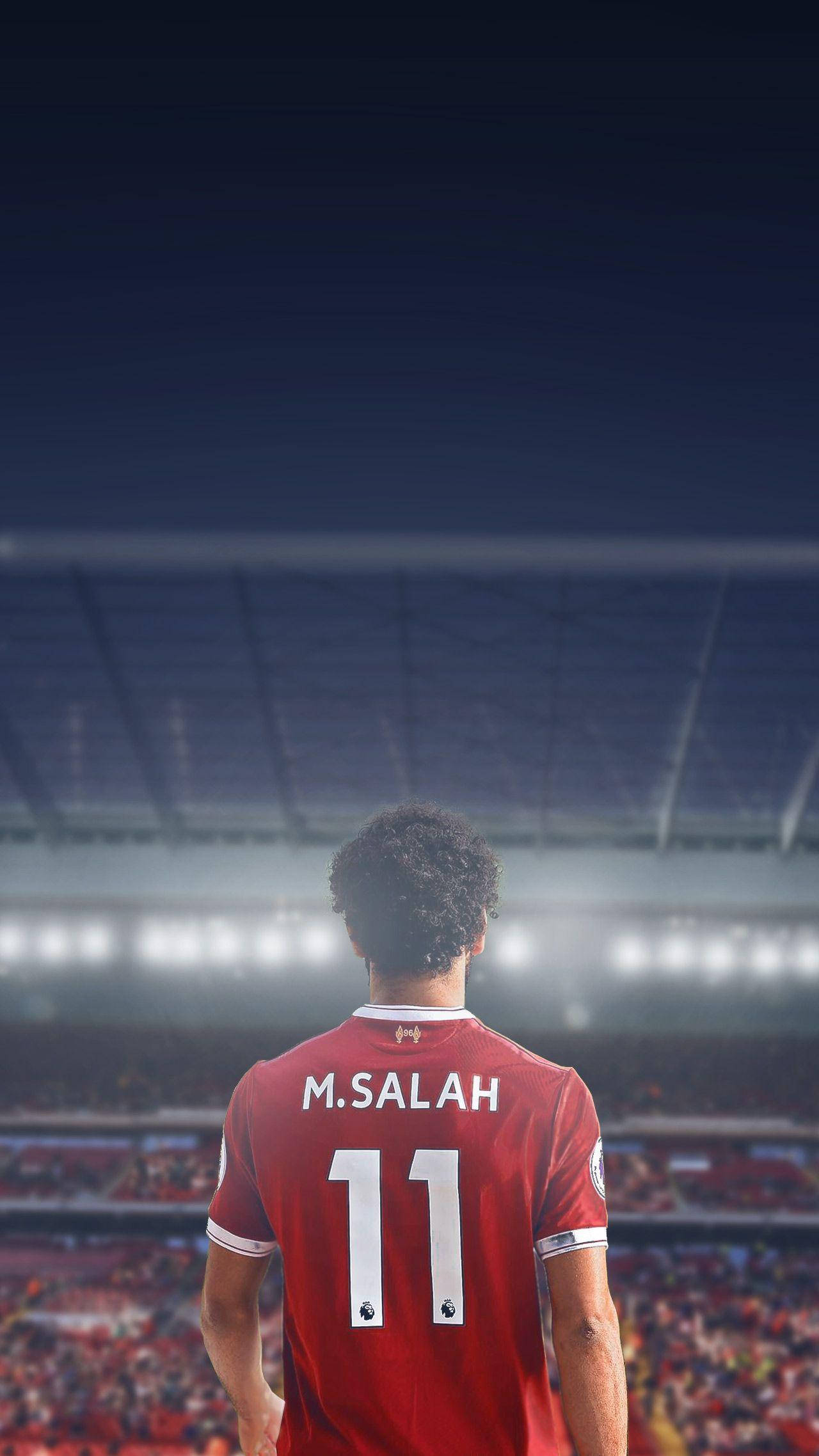 Salah 桌布 壁紙 — 一名身穿紅色球衣、背後印有M SALAH 11的足球員，獨自站在明亮的燈光下廣闊的球場上。