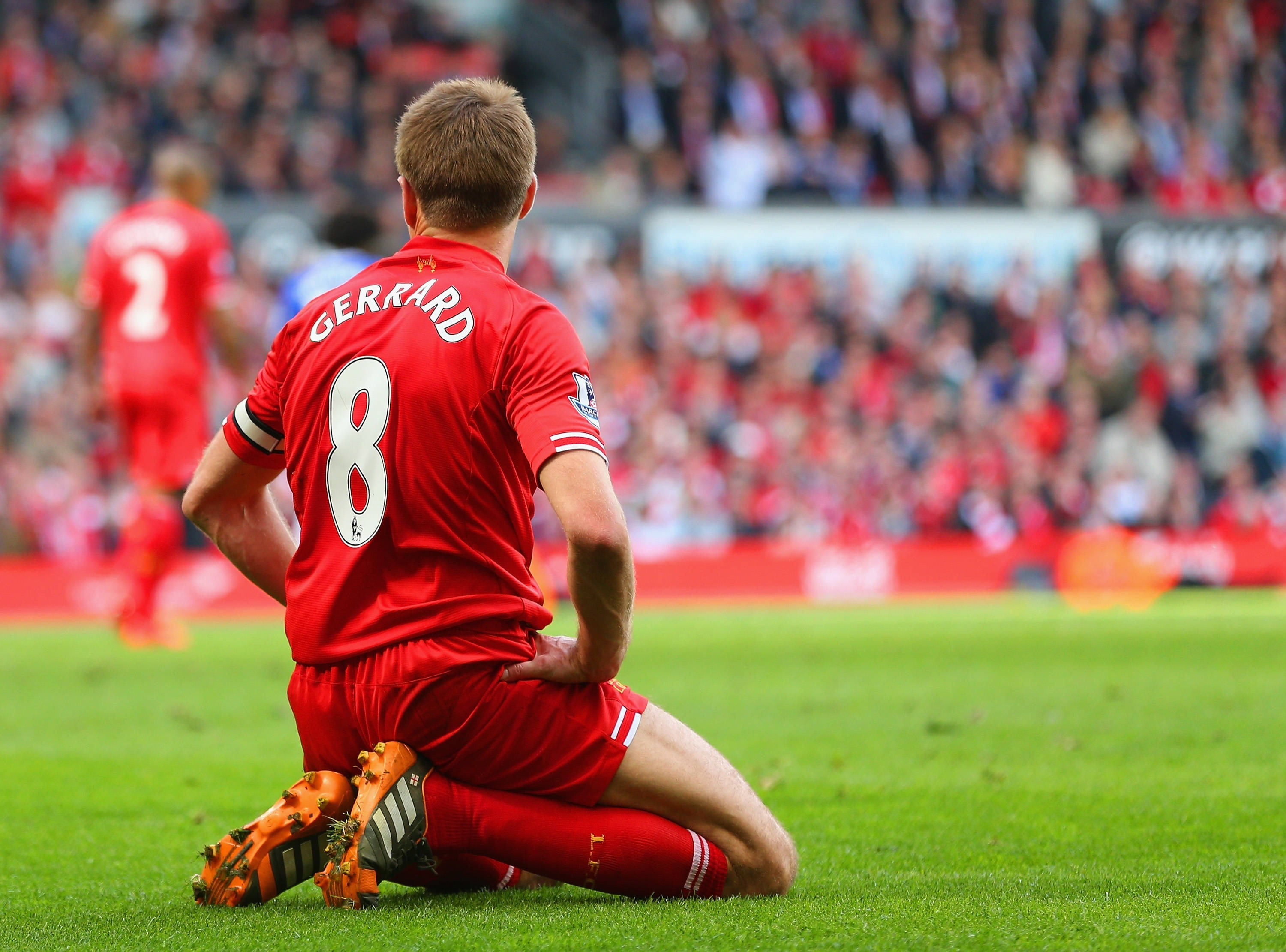 Steven Gerrard 桌布 壁紙 — 一名身穿紅色球衣、號碼8的足球員跪在充滿活力的綠色球場上，面向模糊的人群。
