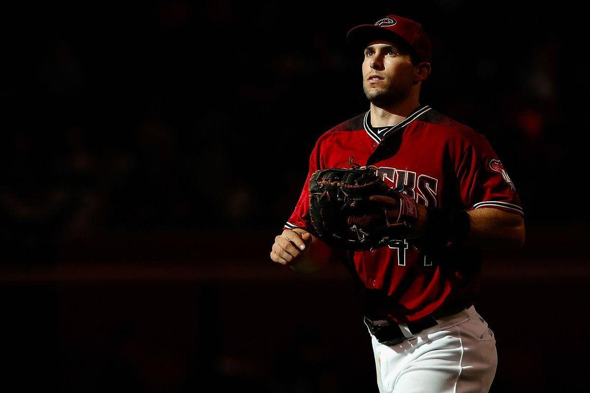 Paul Goldschmidt 桌布 壁紙 — 一名身穿紅色球衣和帽子的棒球運動員在黑暗的球場背景下，專注地站在明亮的聚光燈下。