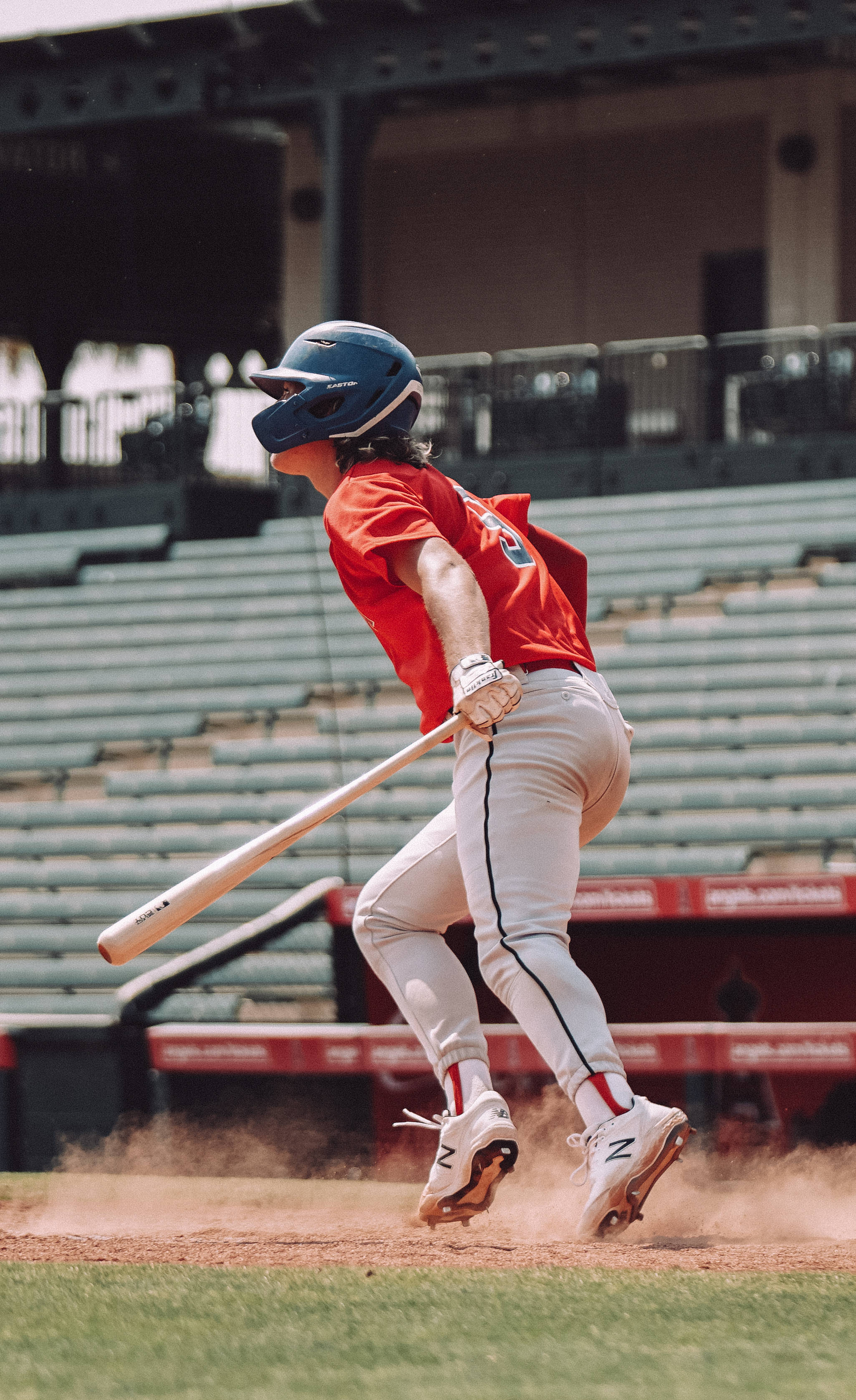 MLB 桌布 壁紙 — 一名身穿紅色球衣和藍色頭盔的棒球手在陽光燦爛的日子裡在球場上揮棒擊球，揚起塵土。