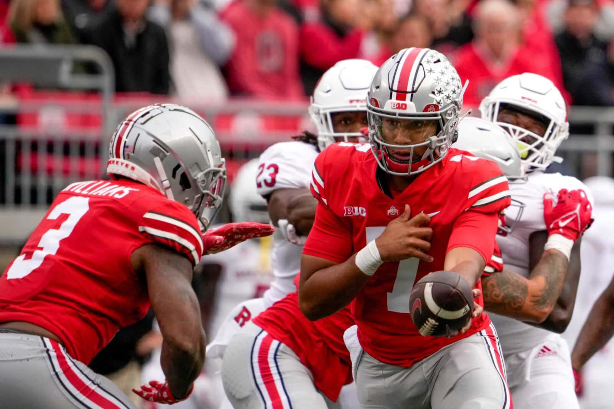 Cool Ohio State 桌布 壁紙 — 一名身穿紅色球衣和銀色頭盔的美式足球四分衛在緊張的比賽中，在防守球員逼近時持球衝刺。
