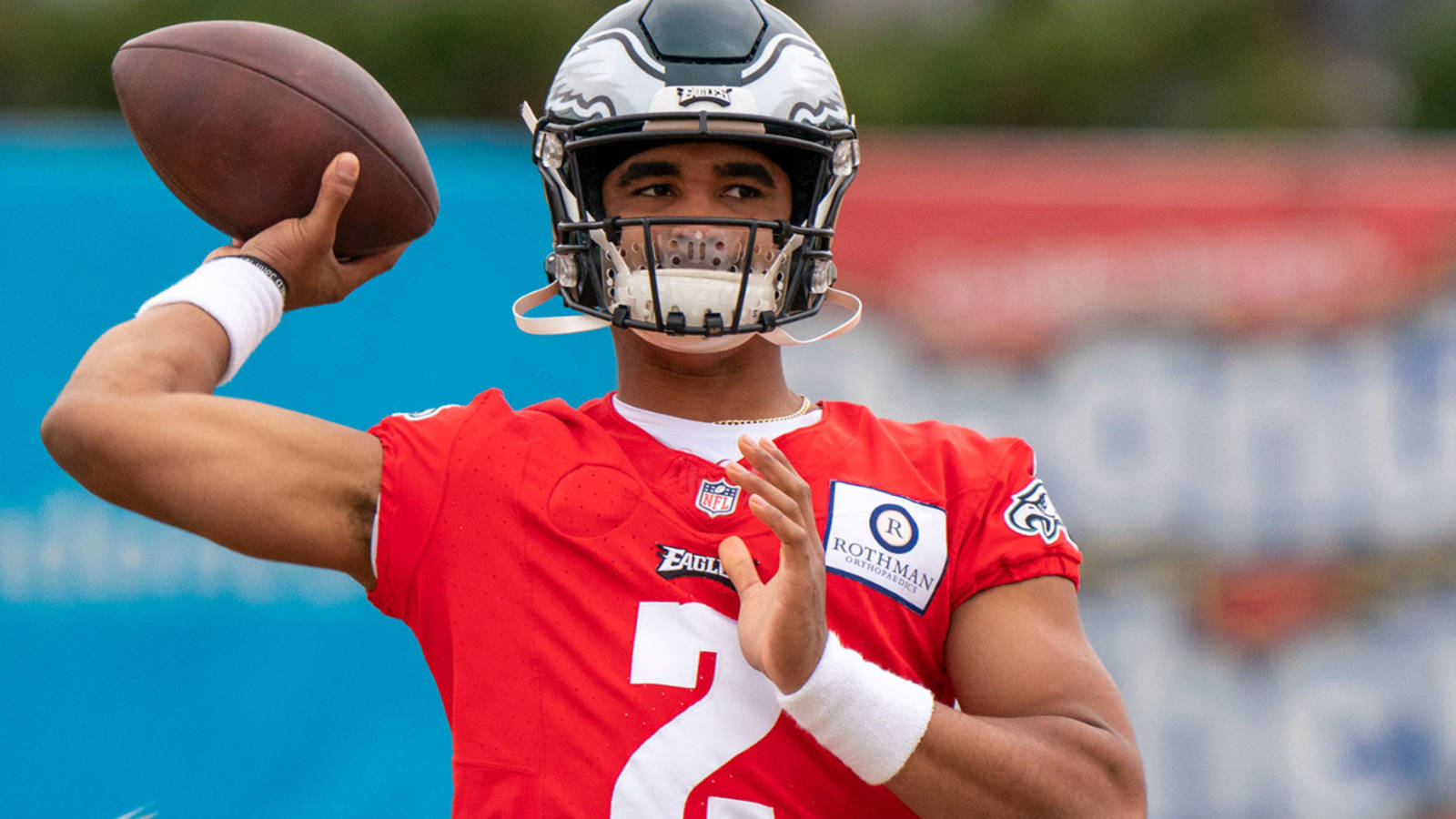Jalen Hurts Eagles 桌布 壁紙 — 一名身穿紅色球衣和頭盔的美式足球四分衛在陽光明媚的戶外練習中準備投球。