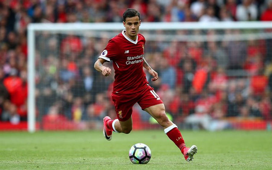 Philippe Coutinho 桌布 壁紙 — 一名身穿紅色球衣的利物浦足球員在充滿活力的綠色球場上盤球，背景有模糊的人群和球門。