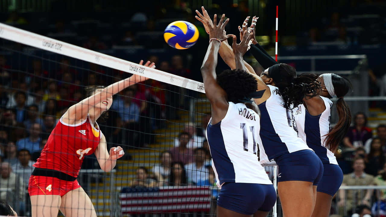 Volleyball 桌布 壁紙 — 一名身穿紅色球衣的女排球員扣球，三名身穿藍白色球衣的對手在網前跳起攔網。