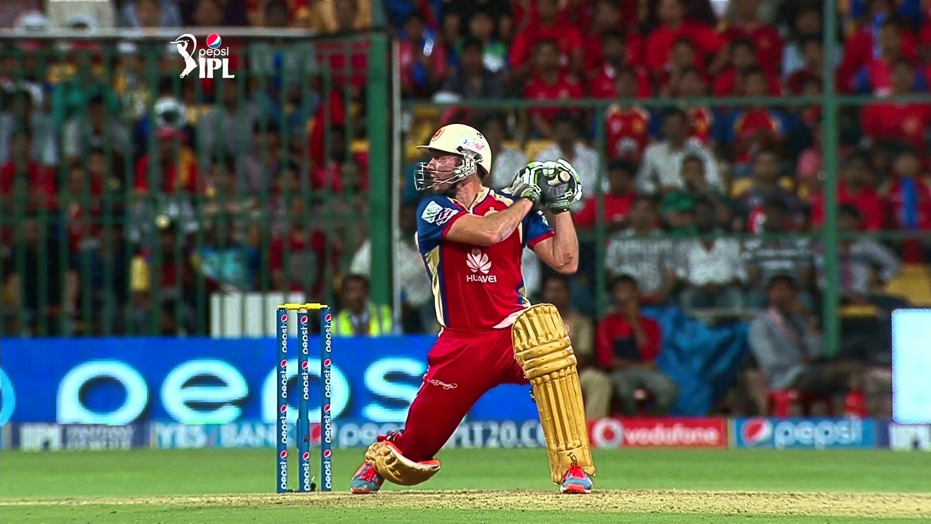 royal challengers bangalore 桌布 壁紙 — 一名身穿紅色球衣的板球擊球手在夜間比賽中，於球場燈光下強力揮棒，背景有歡呼的球迷。