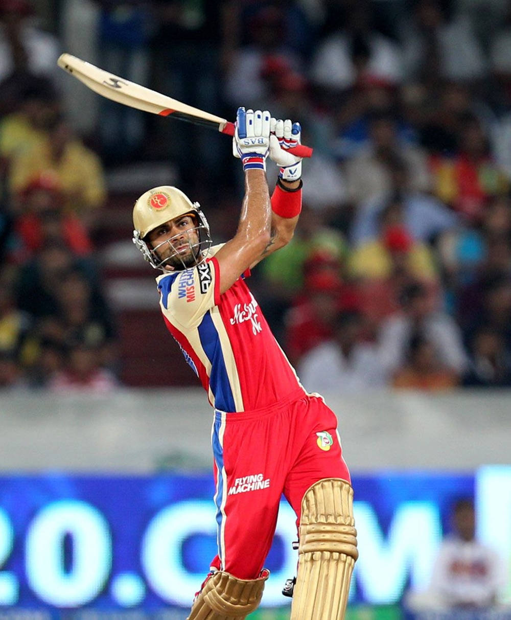 royal challengers bangalore 桌布 壁紙 — 一名身穿紅色球衣的板球擊球手在夜間比賽中，在球場燈光下強力揮動球棒。