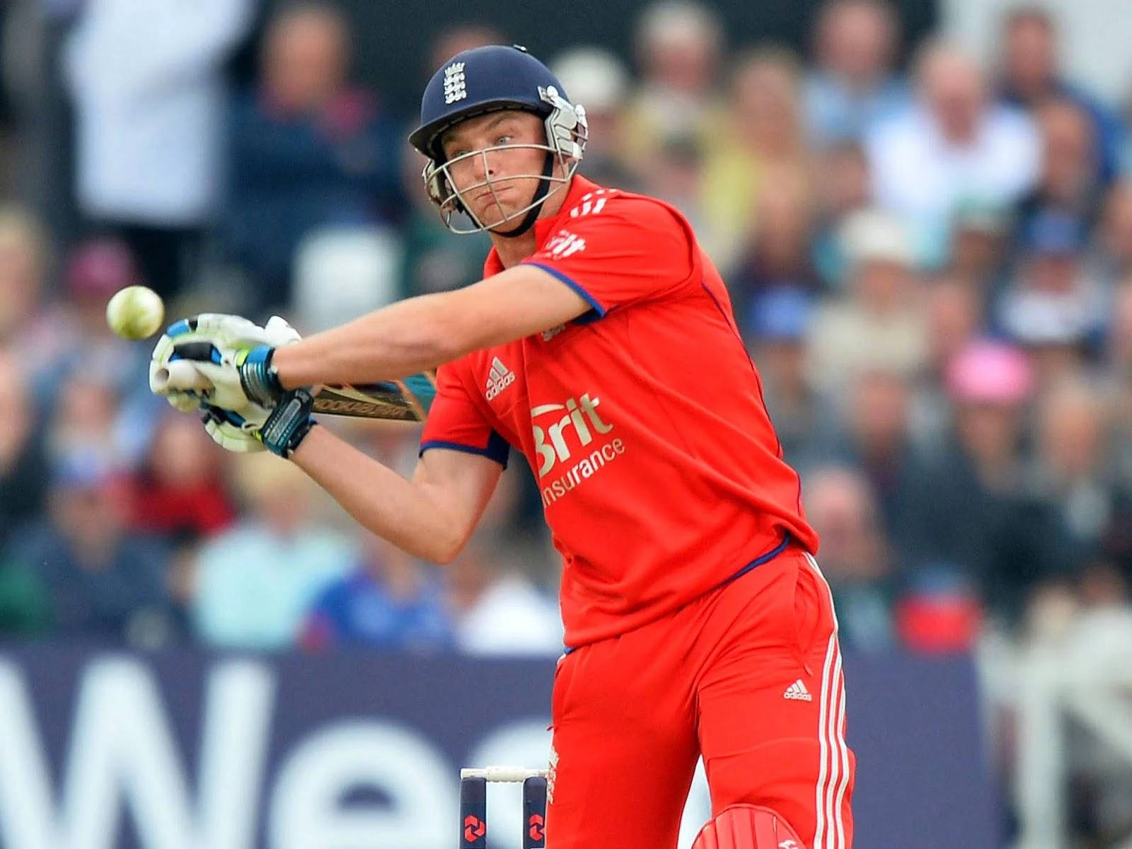 jos buttler 桌布 壁紙 — 一名身穿紅色球衣的板球運動員在日間比賽中揮動球棒擊球，背景是模糊的人群。