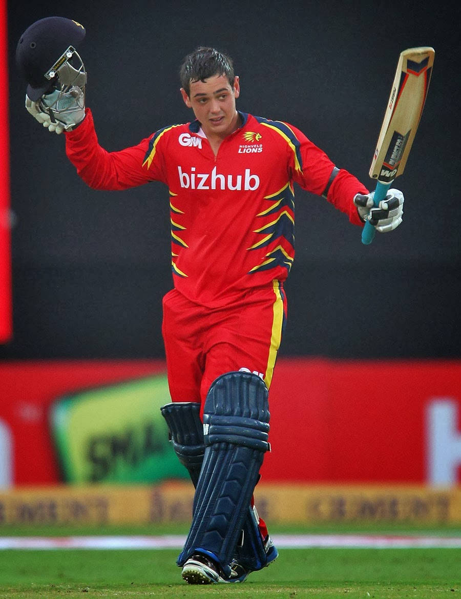 quinton de kock 桌布 壁紙 — 一名身穿紅色球衣的板球運動員在體育場燈光下的綠色場地上舉起球棒和頭盔慶祝。