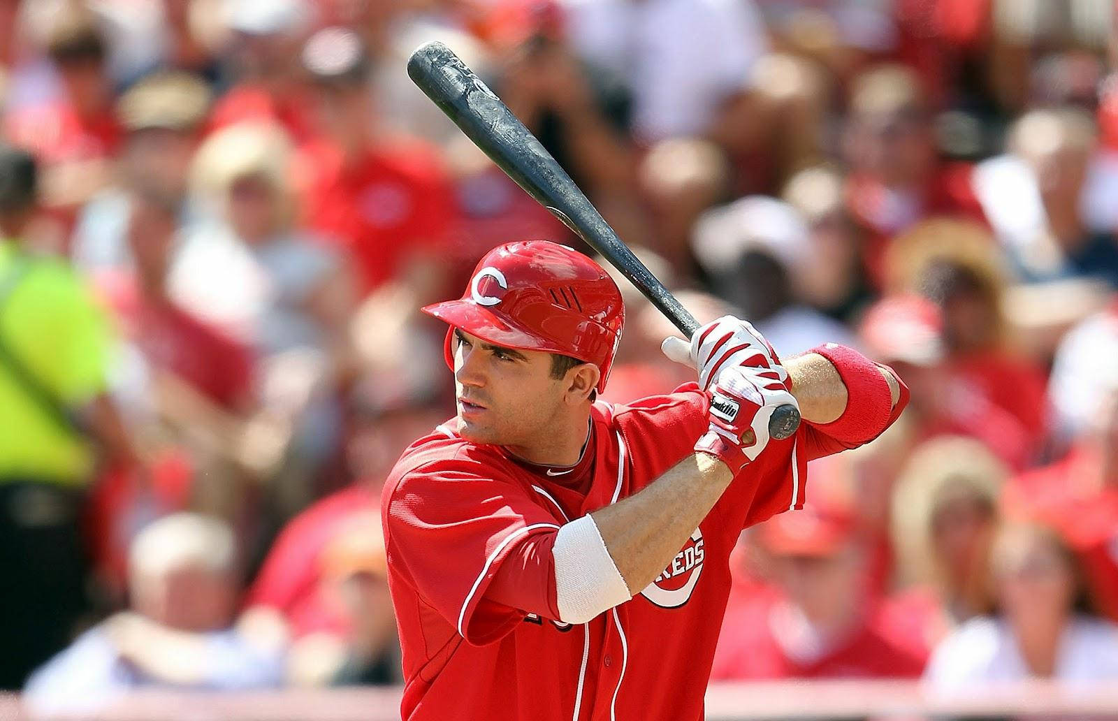 Joey Votto 桌布 壁紙 — 一名身穿紅色球衣的棒球運動員在日間比賽中，背景是模糊的人群，他全神貫注地揮棒。