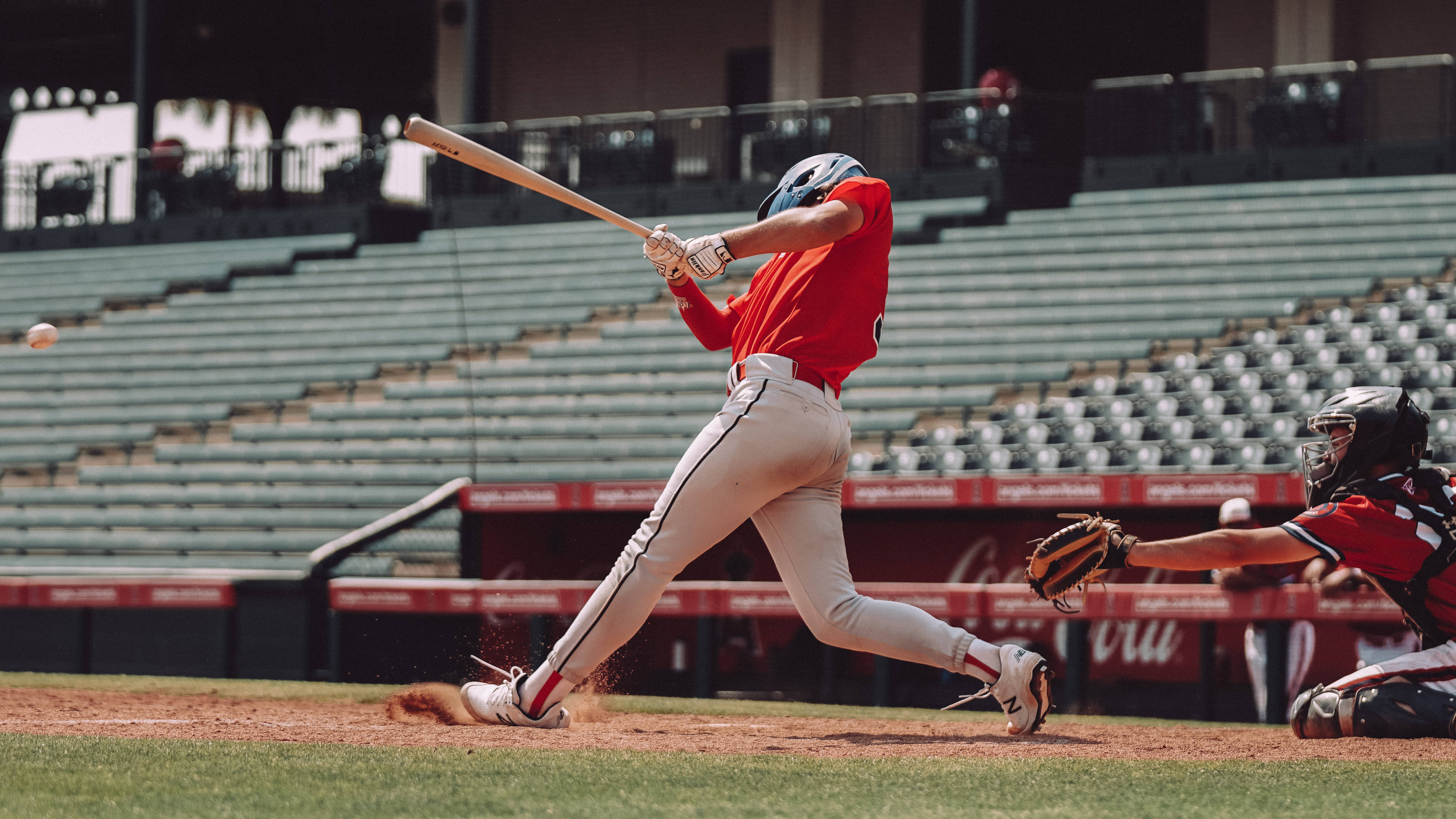 Softball 桌布 壁紙 — 一名身穿紅色球衣的棒球選手在空無一人的球場上，專注地揮棒擊球，捕手蹲在他身後。