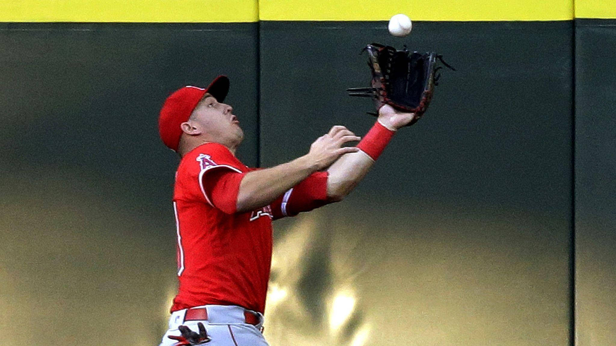 Mike Trout 桌布 壁紙 — 一名身穿紅色球衣的棒球選手跳起，用他的手套接住一個白色的球，背景是黃色和深綠色的牆壁。