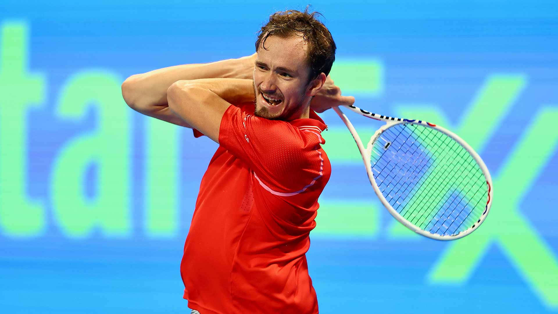 HD Tennis 桌布 壁紙 — 一名身穿紅色球衣的男網球選手，在藍綠色品牌背景前，以高度專注力執行強力的反手揮拍。