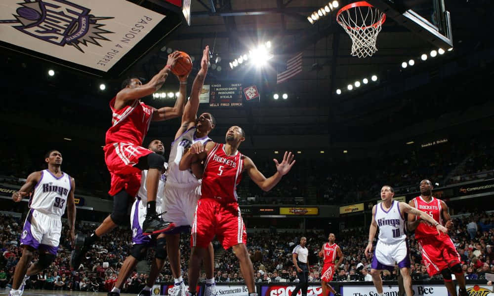 Tracy Mcgrady 桌布 壁紙 — 一名身穿紅色球衣的籃球運動員在場館燈光下跳向籃框，防守球員和隊友圍繞著他。
