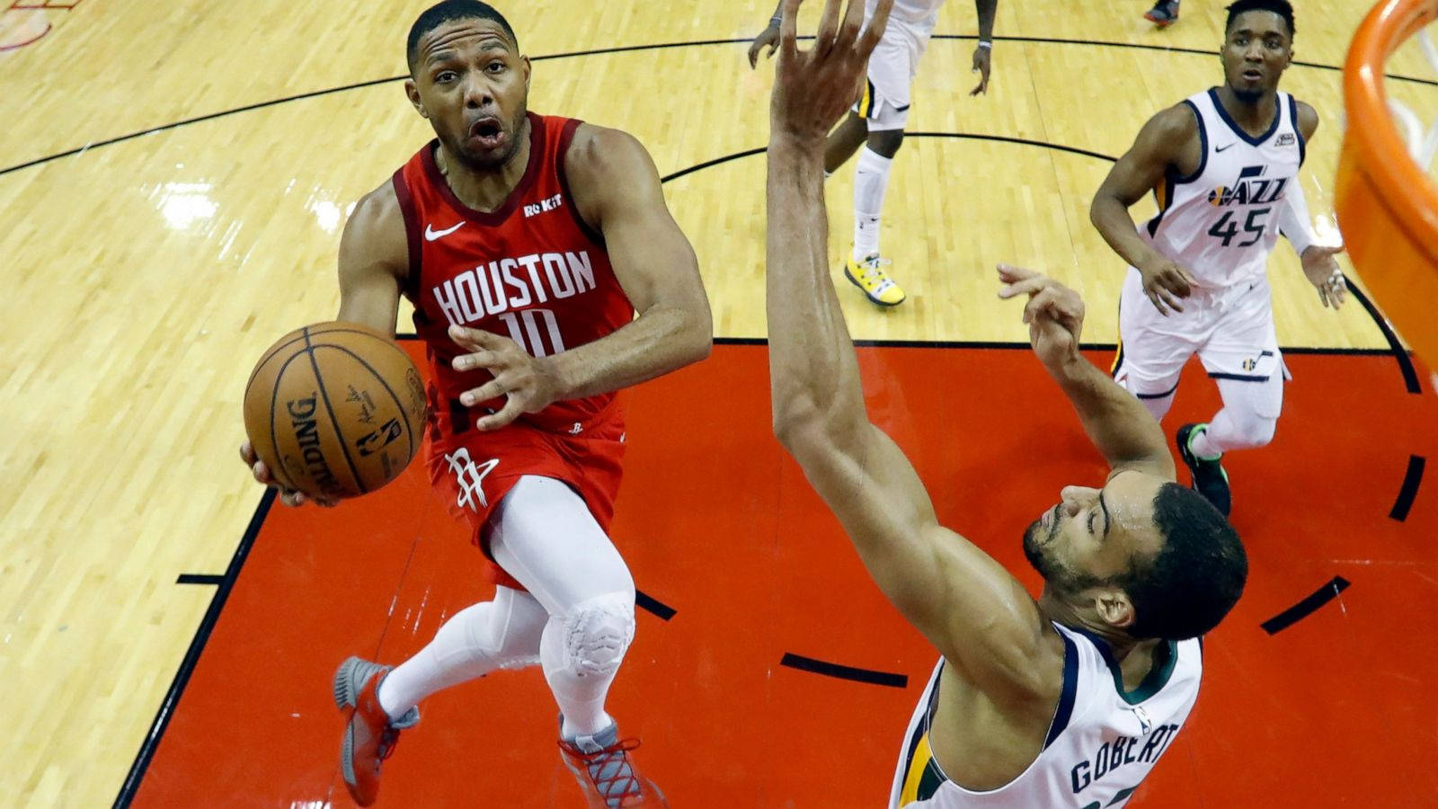eric gordon 桌布 壁紙 — 一名身穿紅色球衣的籃球運動員在激烈的比賽中向籃框切入，防守球員跳起試圖封阻他的投籃。