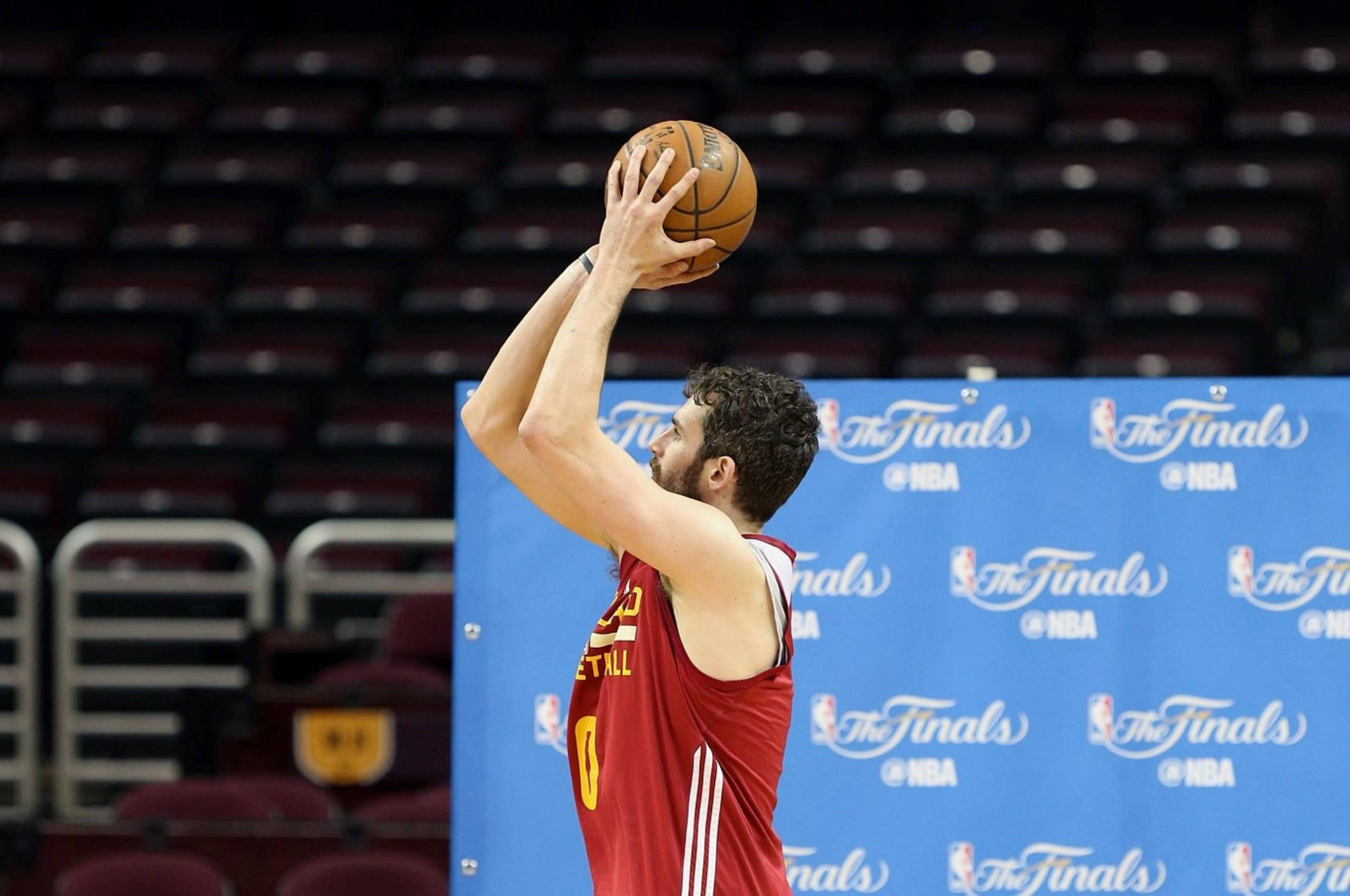 Kevin Love 桌布 壁紙 — 一名身穿紅色球衣的籃球運動員在空蕩的球場上，準備在藍色總決賽背景下投籃。