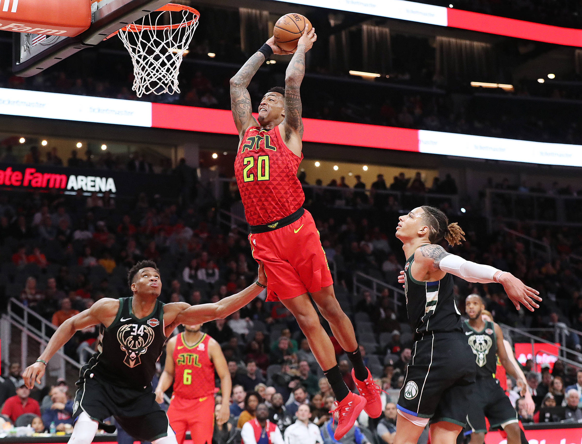 Hawks 桌布 壁紙 — 一名身穿紅色球衣的籃球運動員跳向籃框，而身穿黑色球衣的防守球員試圖在擠滿觀眾的場館比賽中封阻他的投籃。