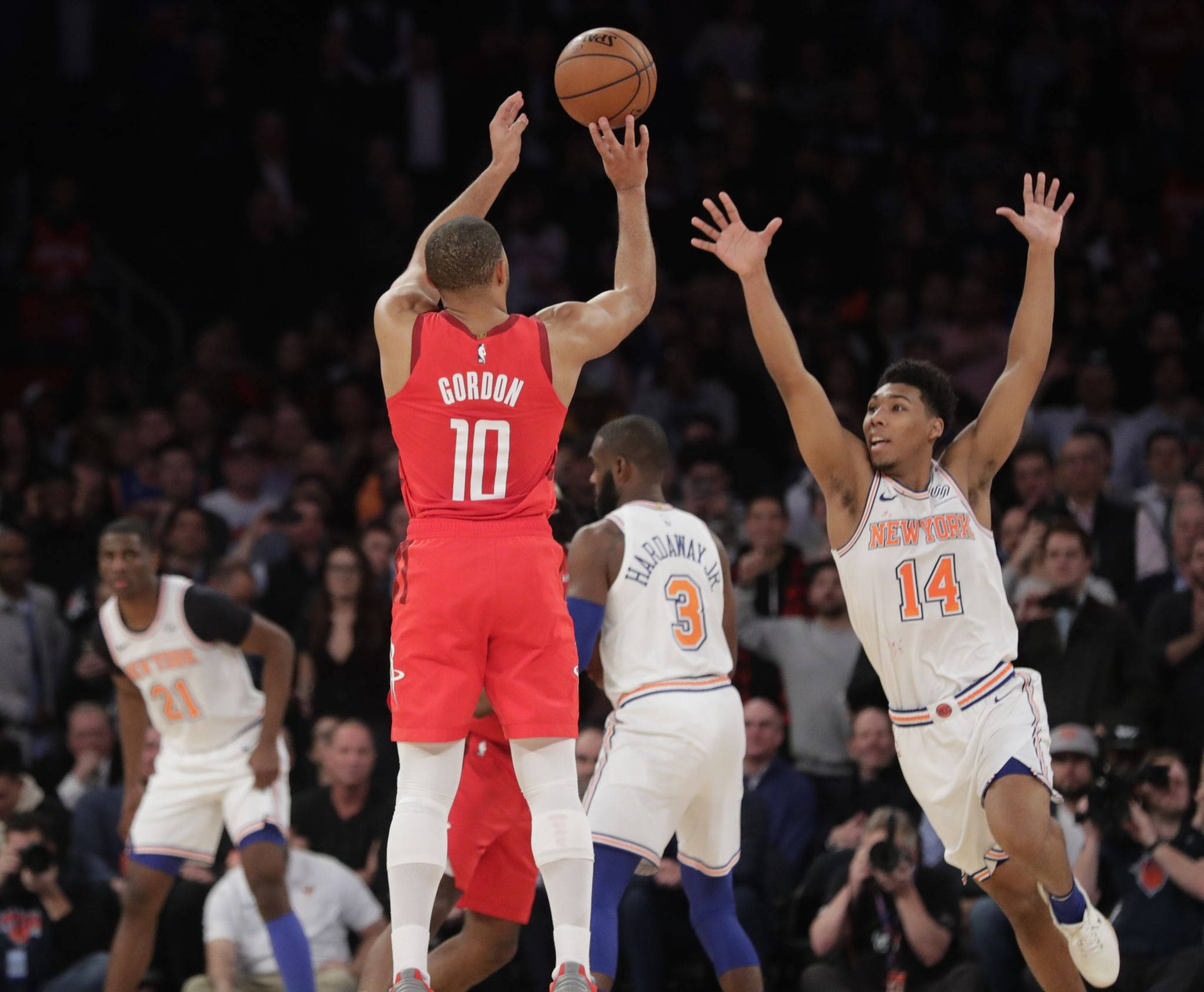 eric gordon 桌布 壁紙 — 一名身穿紅色球衣的籃球運動員跳投，而一名身穿白色球衣的防守球員在場館燈光下跳起封阻。