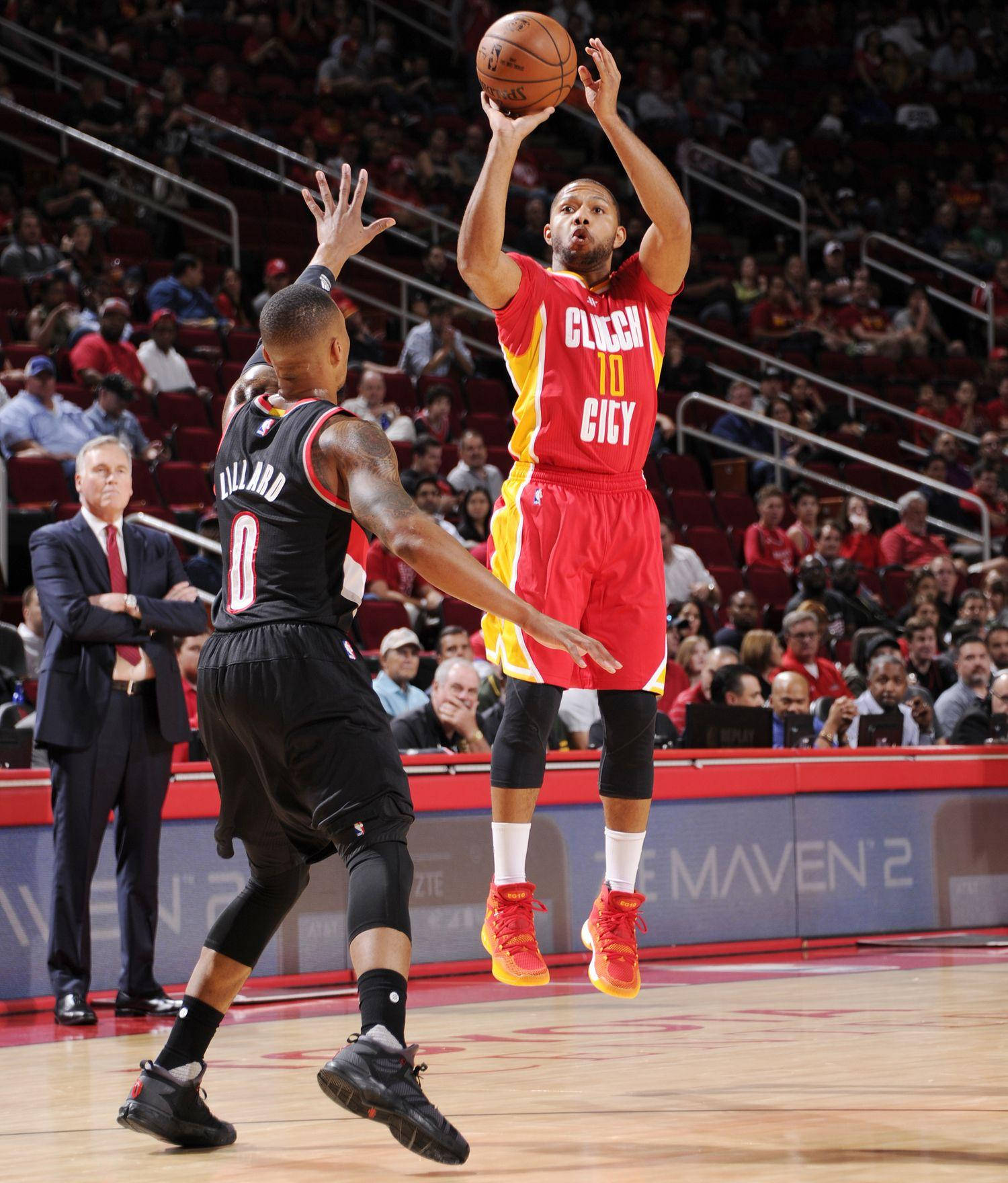 eric gordon 桌布 壁紙 — 一名身穿紅色球衣的籃球運動員跳起投籃，而一名身穿黑色球衣的防守球員在明亮的場館燈光下試圖封阻。