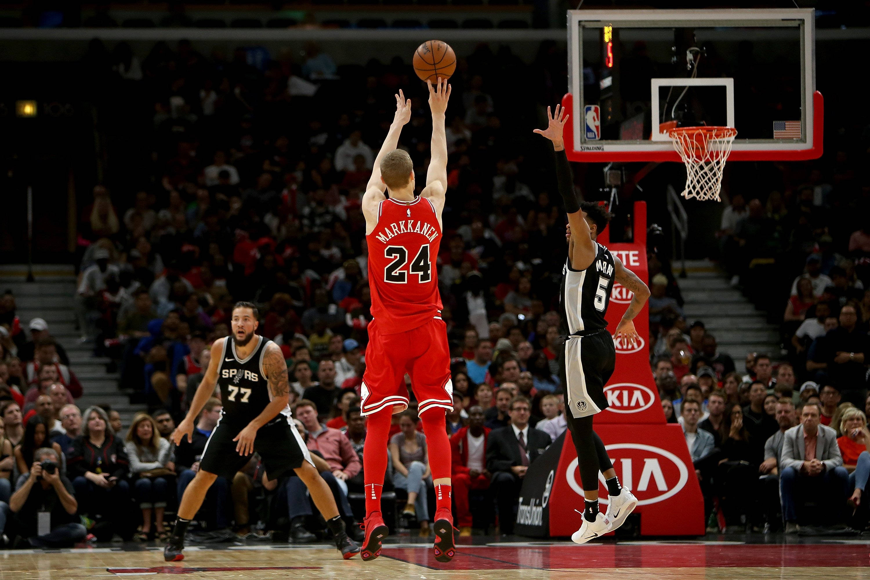 Chicago Bulls 桌布 壁紙 — 一名身穿紅色球衣的籃球運動員跳起投籃，越過一名黑色球衣的防守球員，觀眾們專注地觀看。