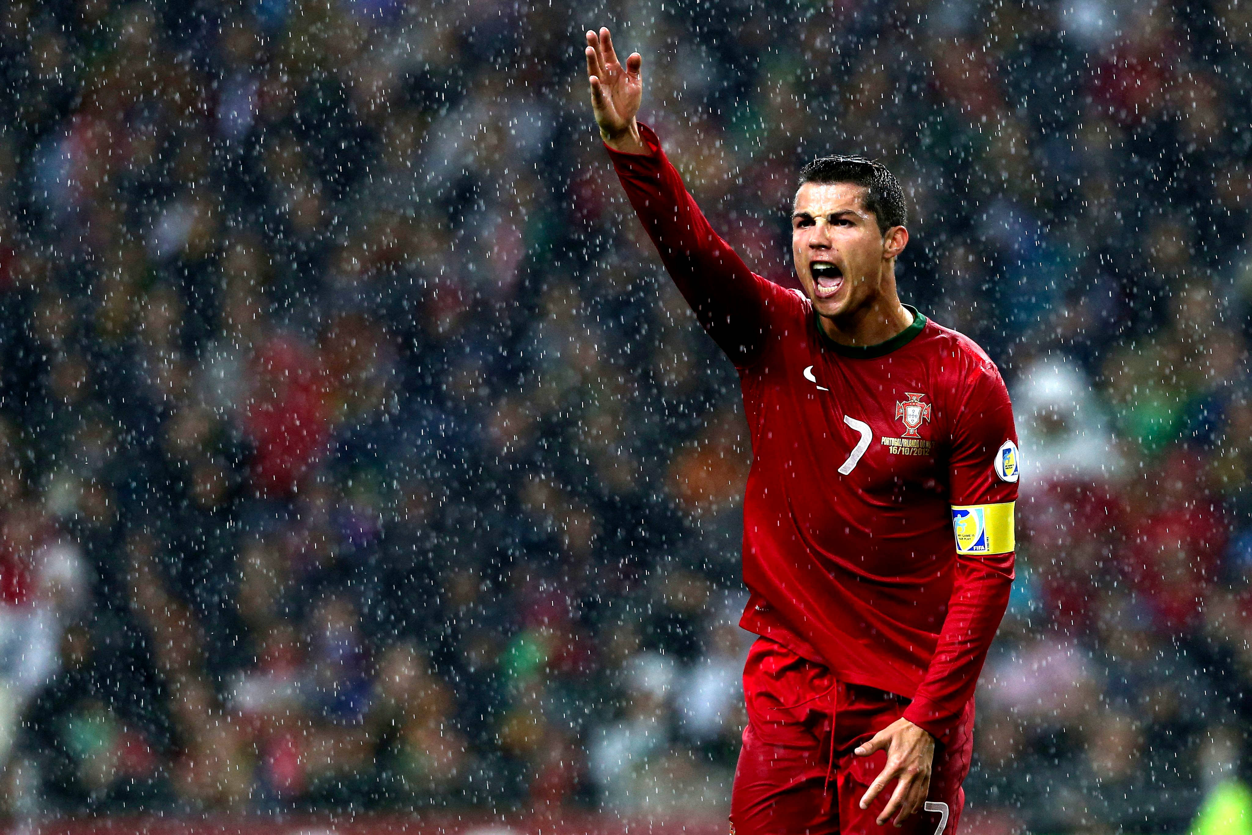 Ronaldo 桌布 壁紙 — 一名身穿紅色球衣的葡萄牙足球員在雨中熱情慶祝，身後的人群模糊不清。