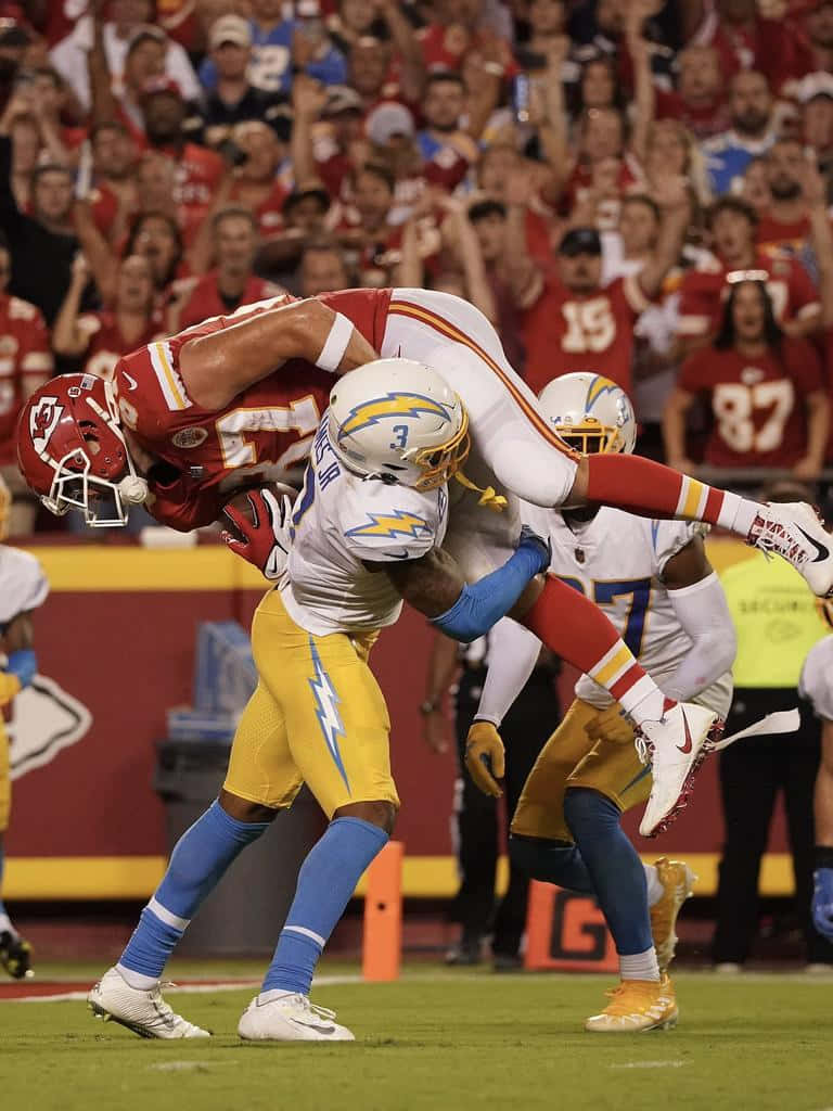 NFL 桌布 壁紙 — 一名身穿紅色球衣的足球員在充滿活力的球場比賽中，向一名身穿白色和黃色球衣、騰空而起的對手進行攔截。