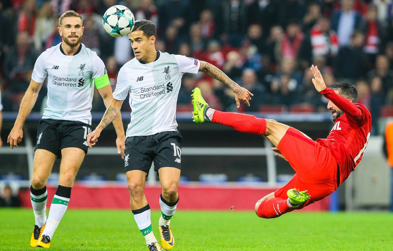 Coutinho 桌布 壁紙 — 一名身穿紅色球衣的足球員在空中做出戲劇性的踢球動作，兩名身穿白色球衣的對手看著球飛過。