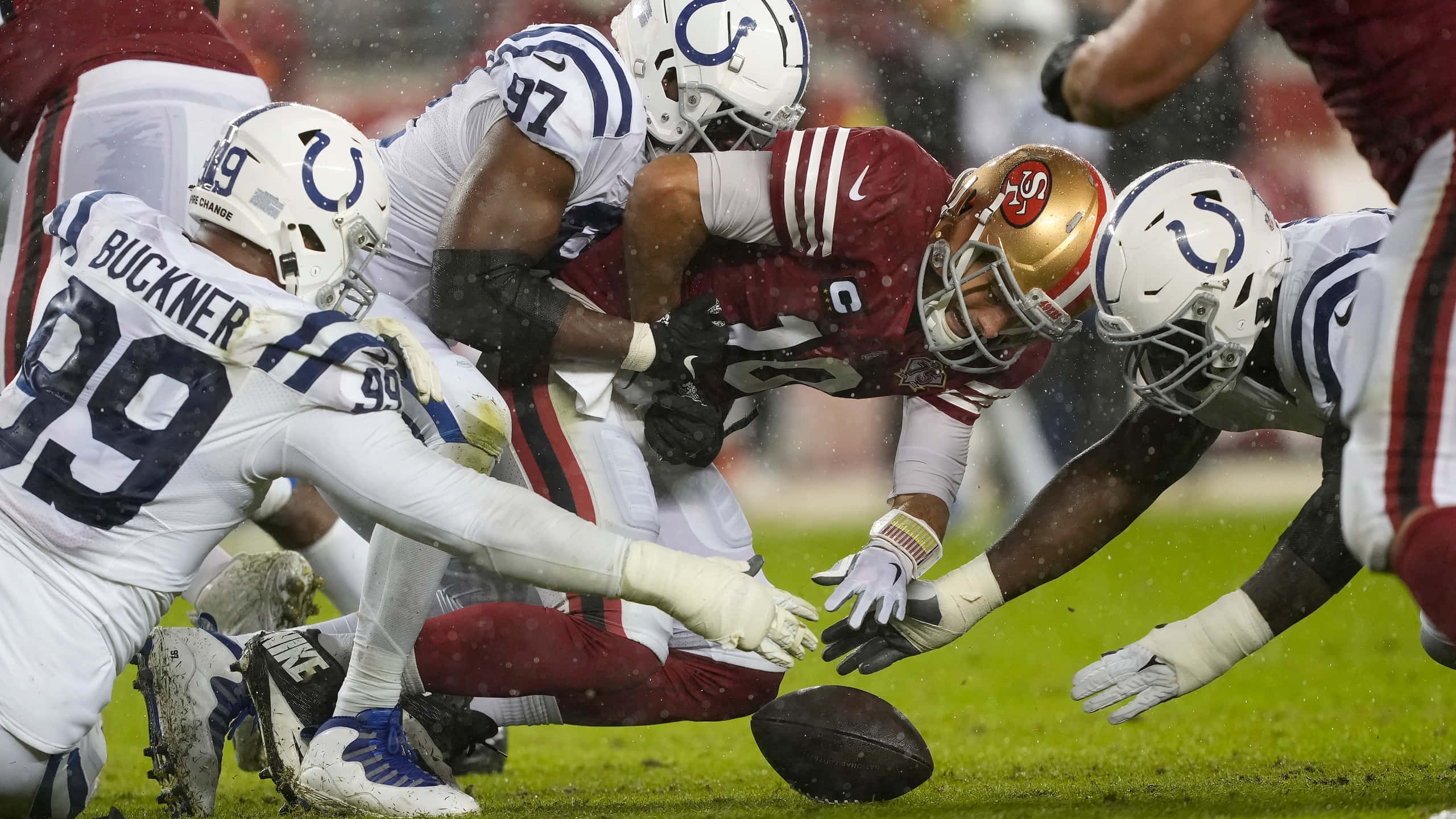 Football Players 桌布 壁紙 — 一名身穿紅色球衣的足球員在雨中球場飛身撲向皮球，白色球衣的防守球員蜂擁而上包圍他。