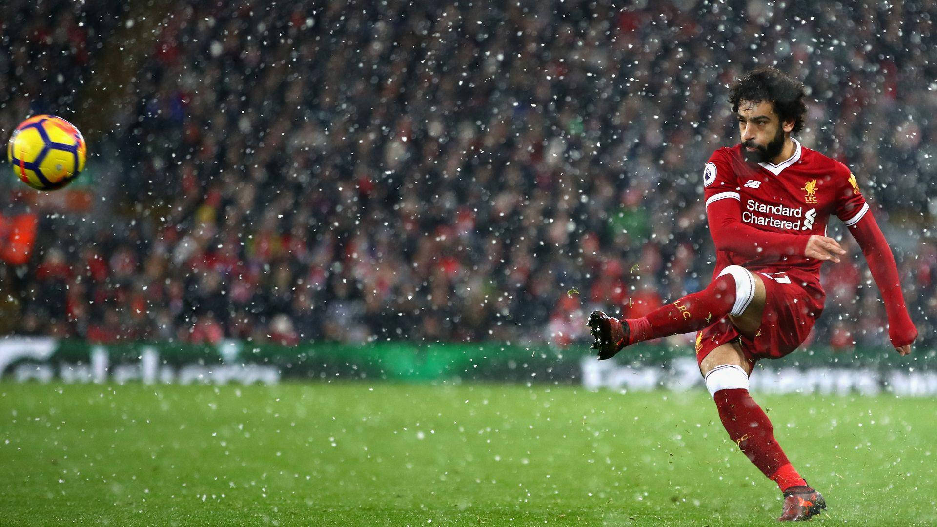 Salah 桌布 壁紙 — 一名身穿紅色球衣的足球員在飄雪中踢著色彩繽紛的球，背景是模糊的觀眾，場地是綠色的草地。