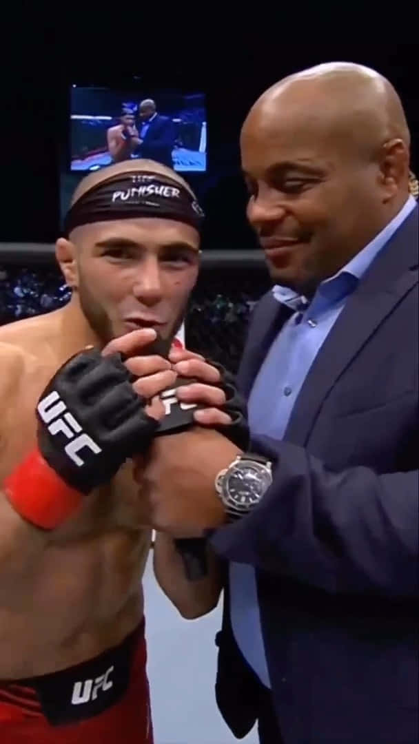 MMA 桌布 壁紙 — 一名身穿紅色短褲和黑色手套的UFC拳手在格鬥賽事中被一名微笑的光頭西裝男擁抱。
